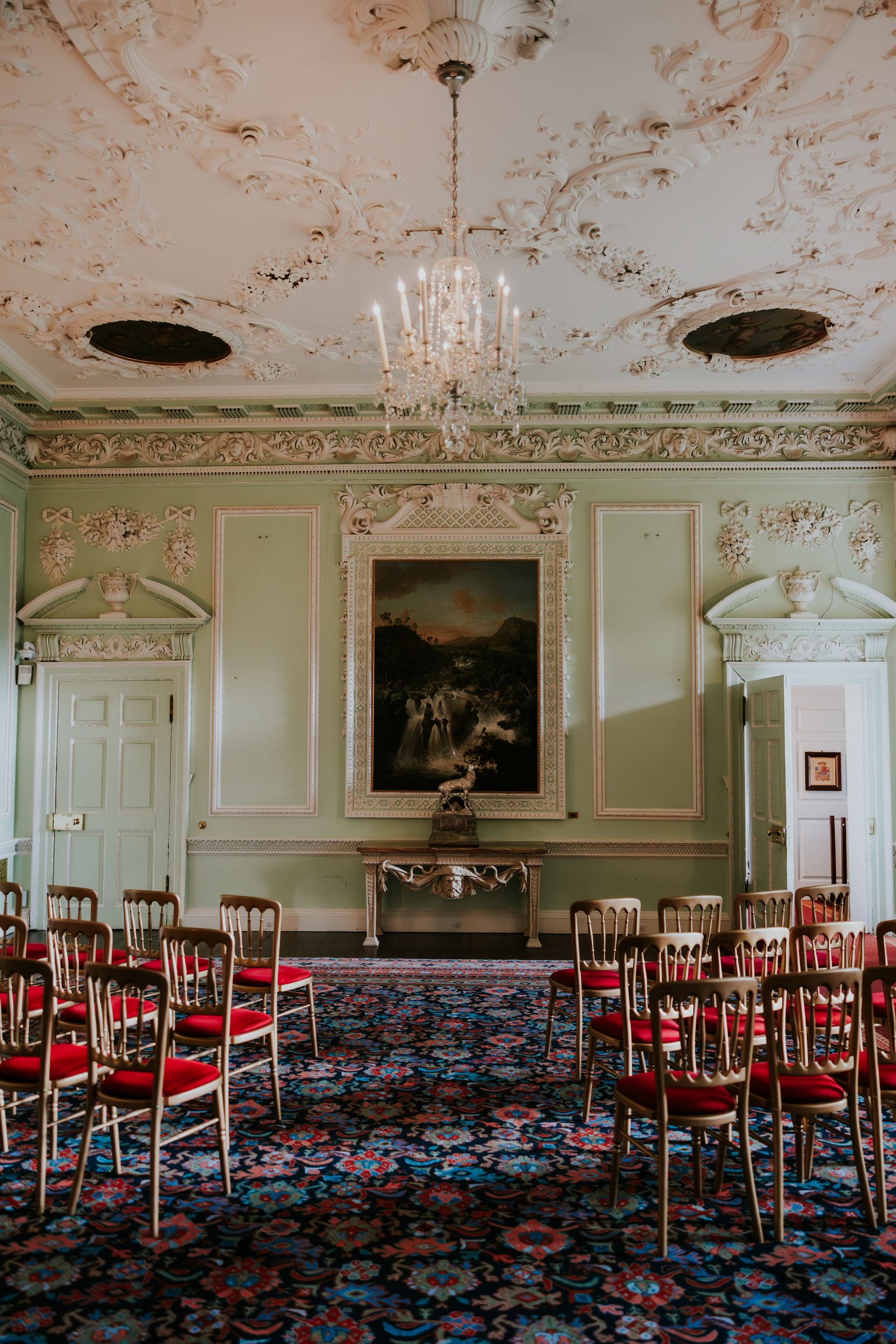 Blair Castle State Dining Room set for a ceremony with crystal chandelier, ornate plaster ceiling and rows of gold chairs with red seats.