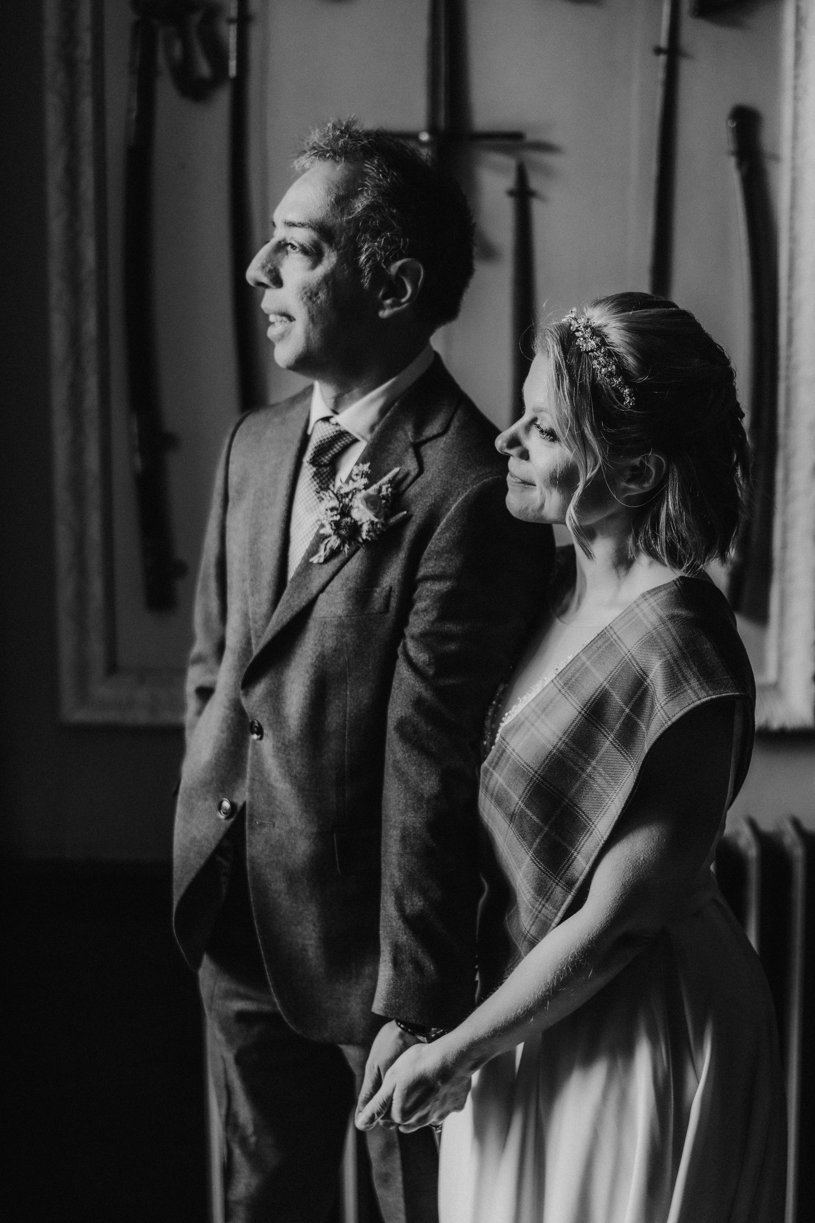 Bride and groom holding hands in profile; bride with tiara and tartan sash, groom in suit with boutonniere.