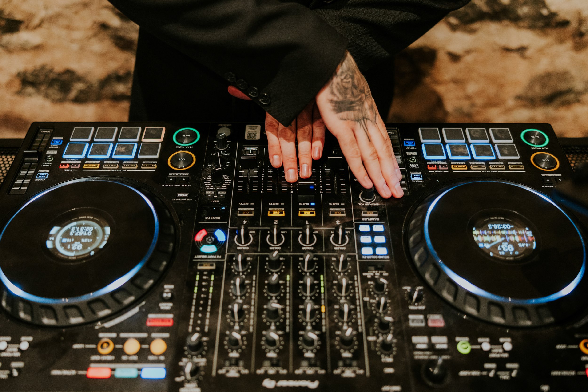 Close-up of DJ decks and mixer with two hands adjusting controls, one hand tattooed.