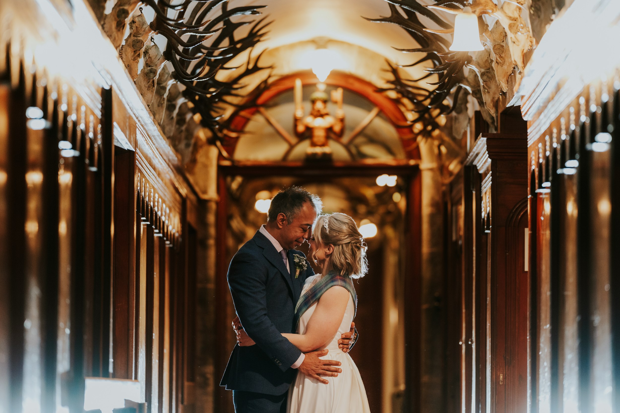 Lizanne and Jitin embrace forehead-to-forehead in an antler-lined wooden corridor.