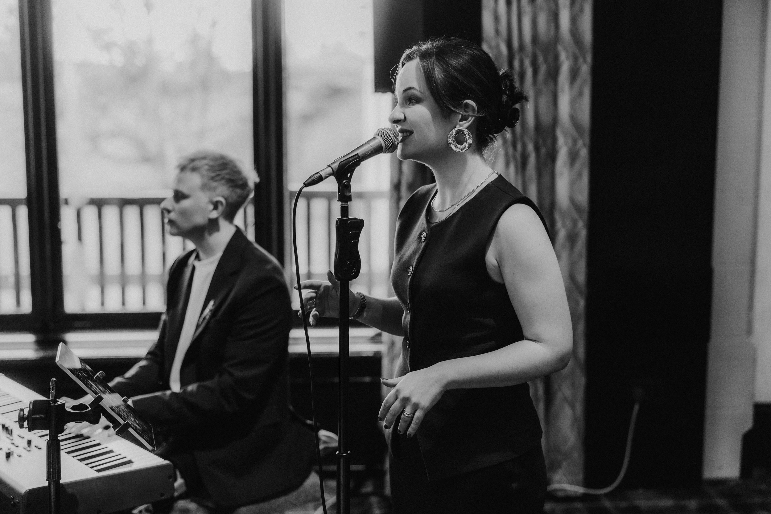 Female singer at a microphone with a keyboard player beside her, performing indoors.