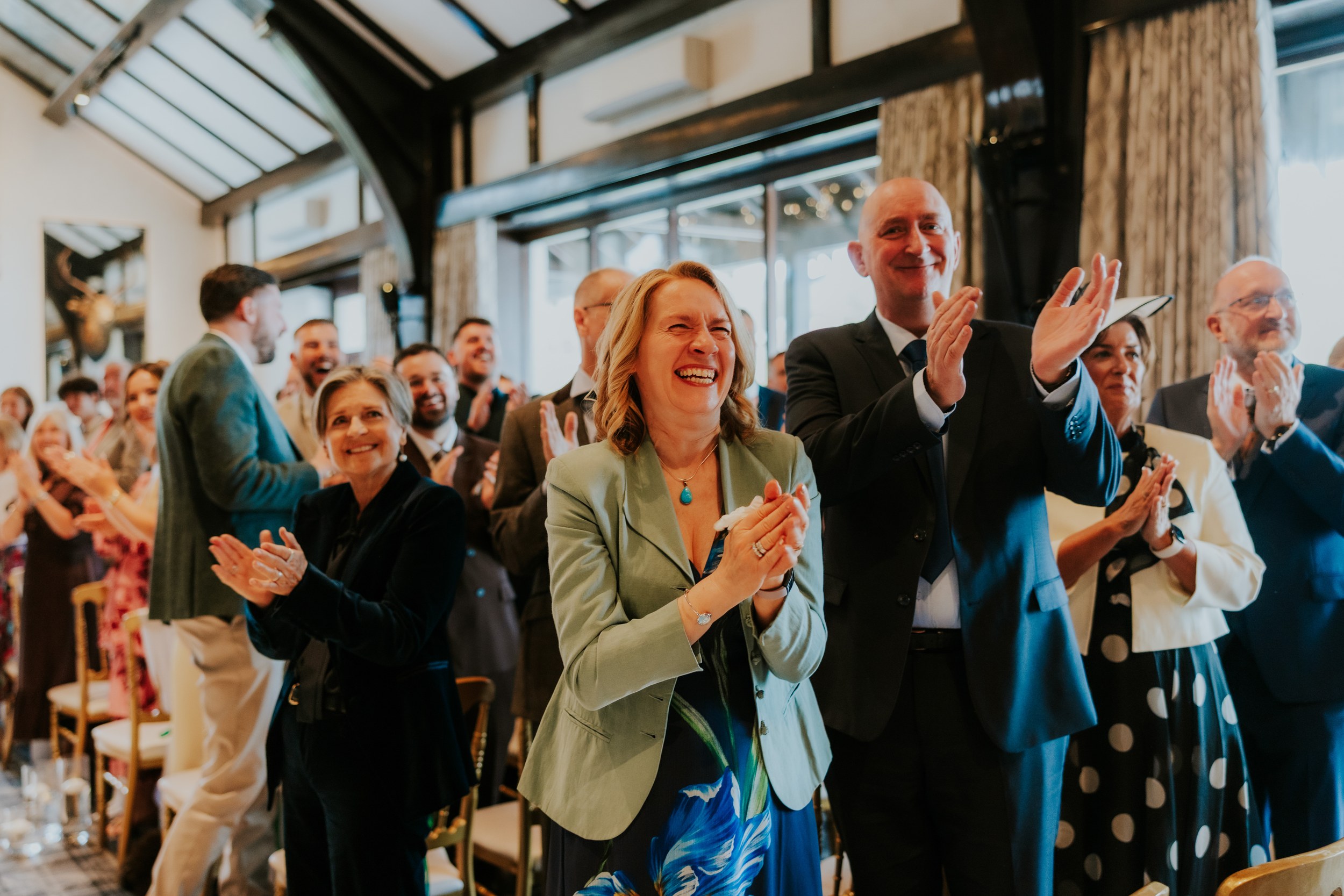 Guests standing and applauding inside a timber‑beamed wedding function room.