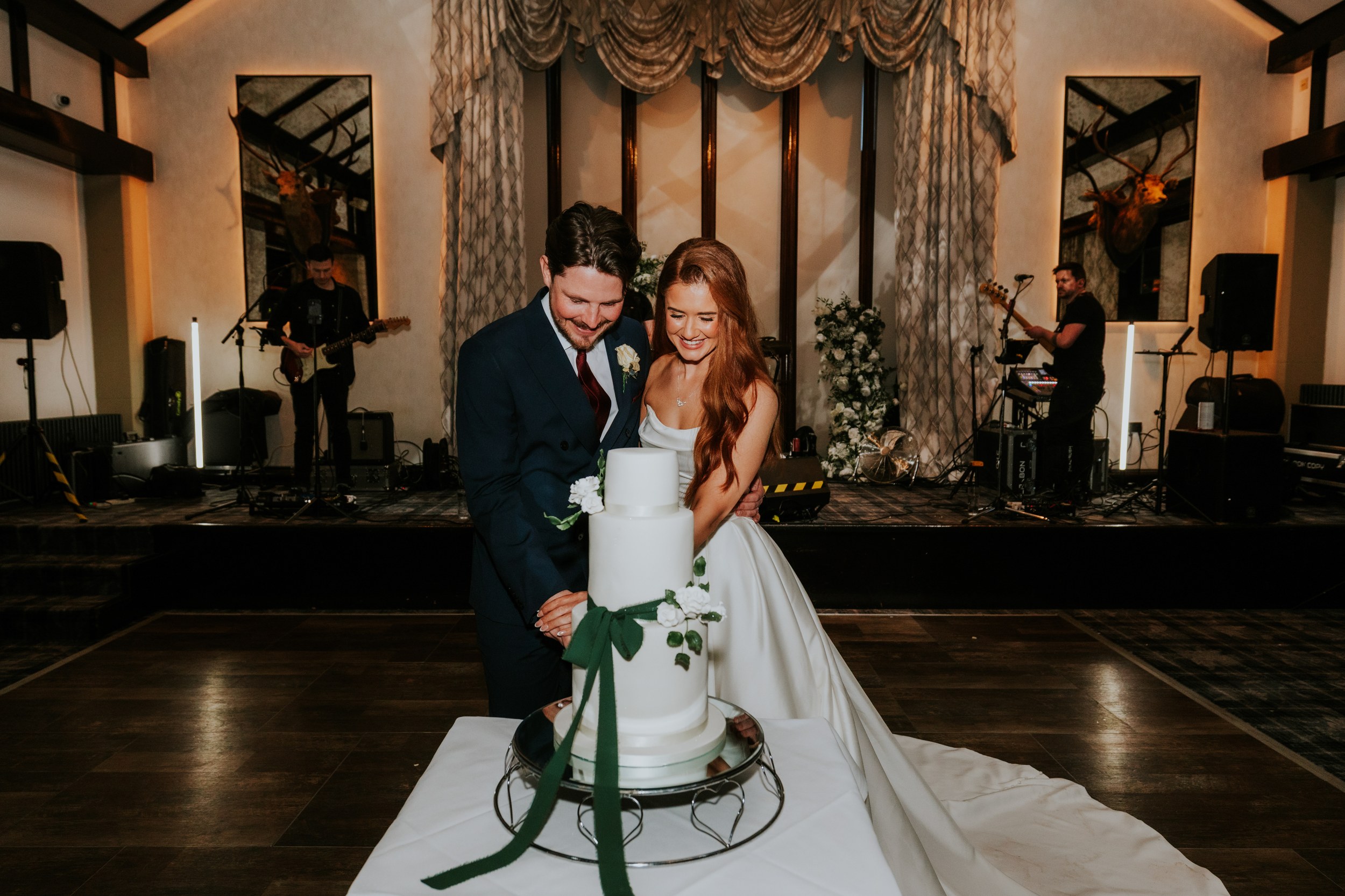 Jack and Robyn cut their four-tier wedding cake in the hotel ballroom with a live band on stage behind them.