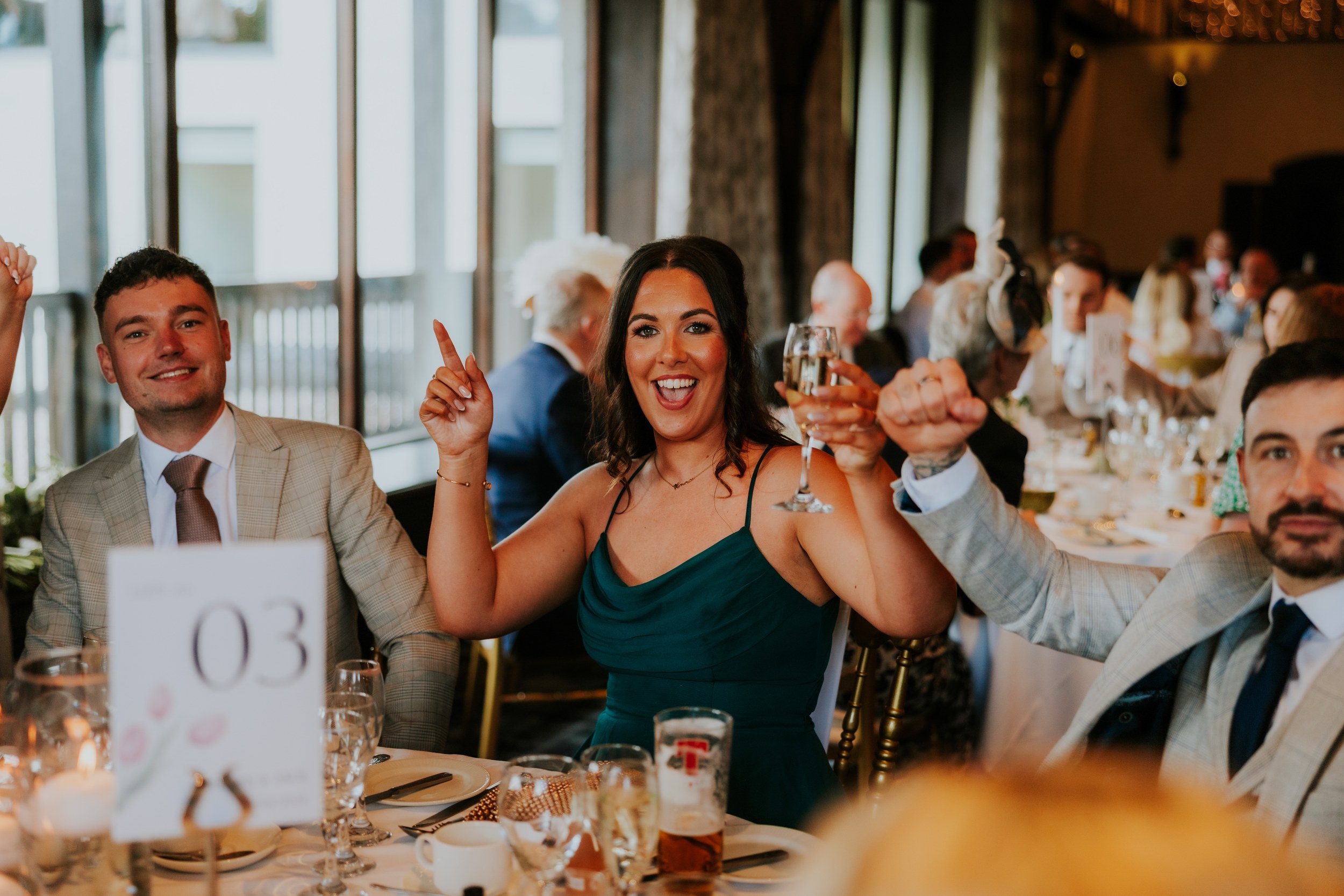 Woman in a green dress smiling and raising a wine glass at a wedding reception table.
