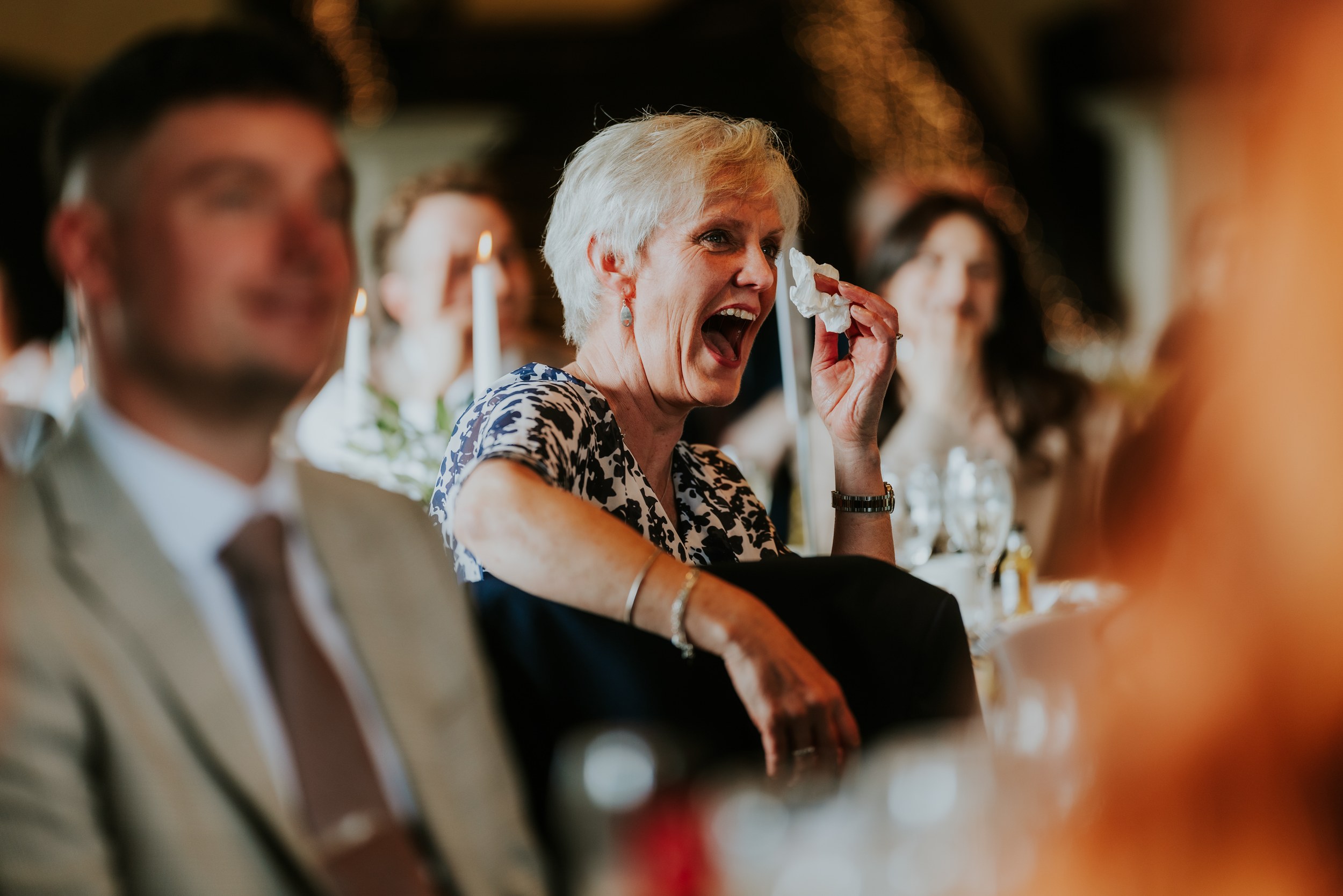 Woman laughing and dabbing her eye with a tissue at a candlelit wedding reception