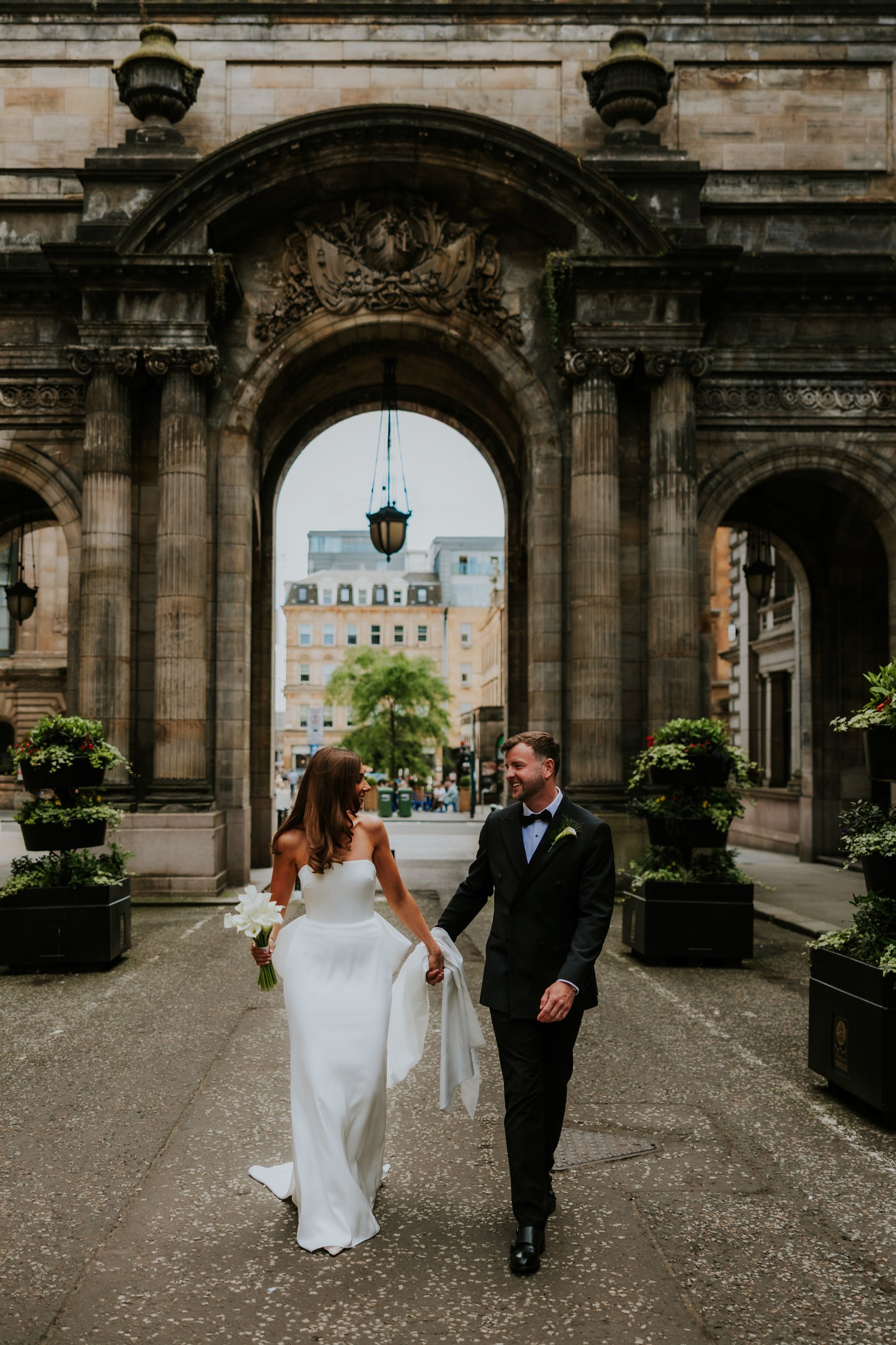 Citation Glasgow wedding photographer 51 Bride and groom holding hands under a stone arch at Citation Glasgow, bride in a white gown with a bouquet.