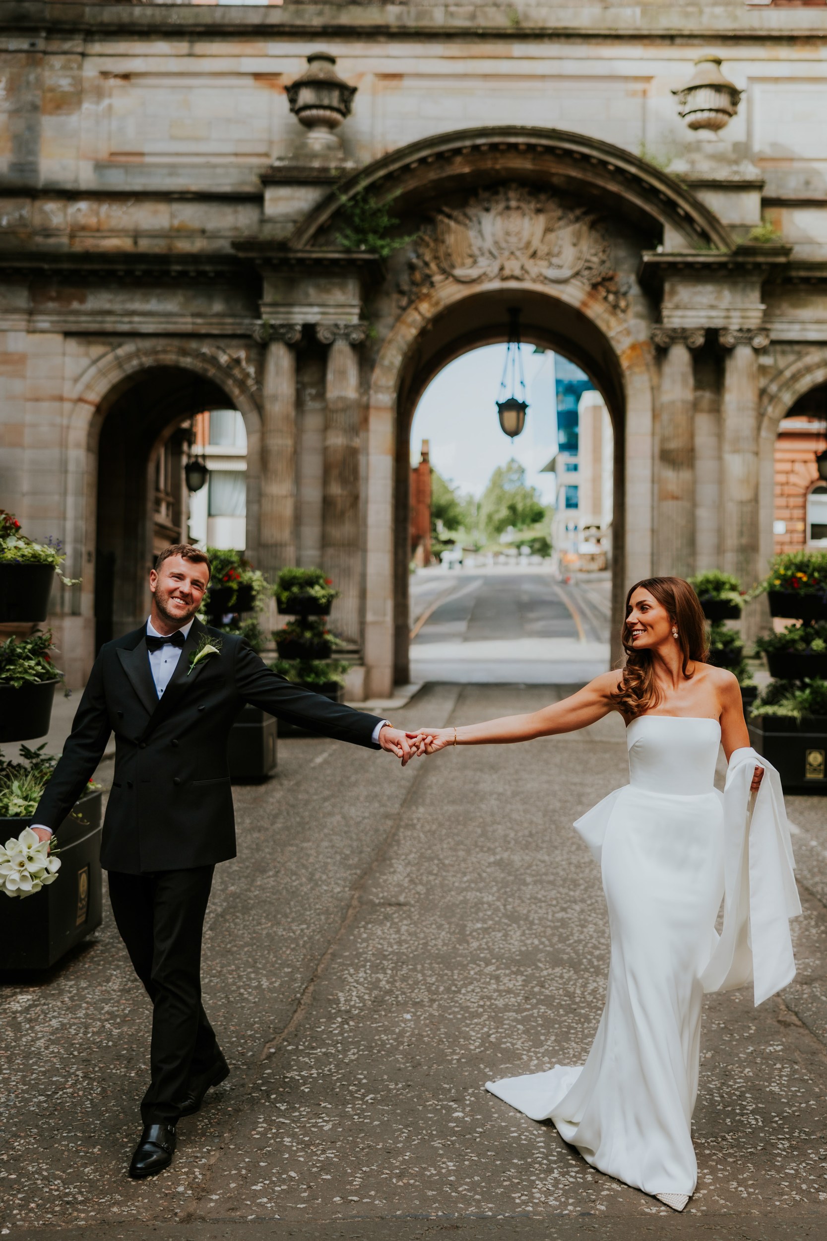 Citation Glasgow wedding photographer 57 Bride and groom holding hands under a stone arch at Citation Glasgow, bride in strapless white dress and groom in a black tuxedo.