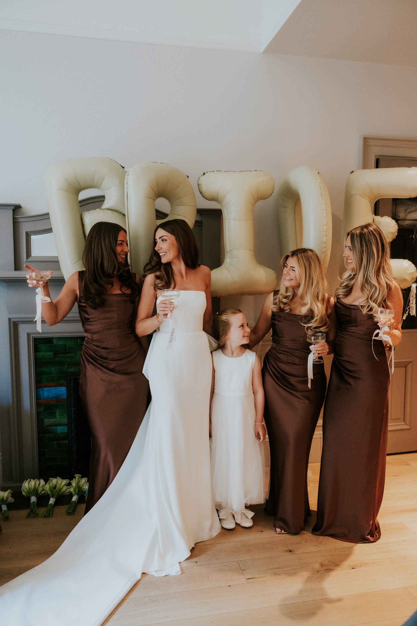 Citation Glasgow wedding photographer 16 Bride and three bridesmaids with a flower girl laughing and toasting in front of gold 'BRIDE' balloons.