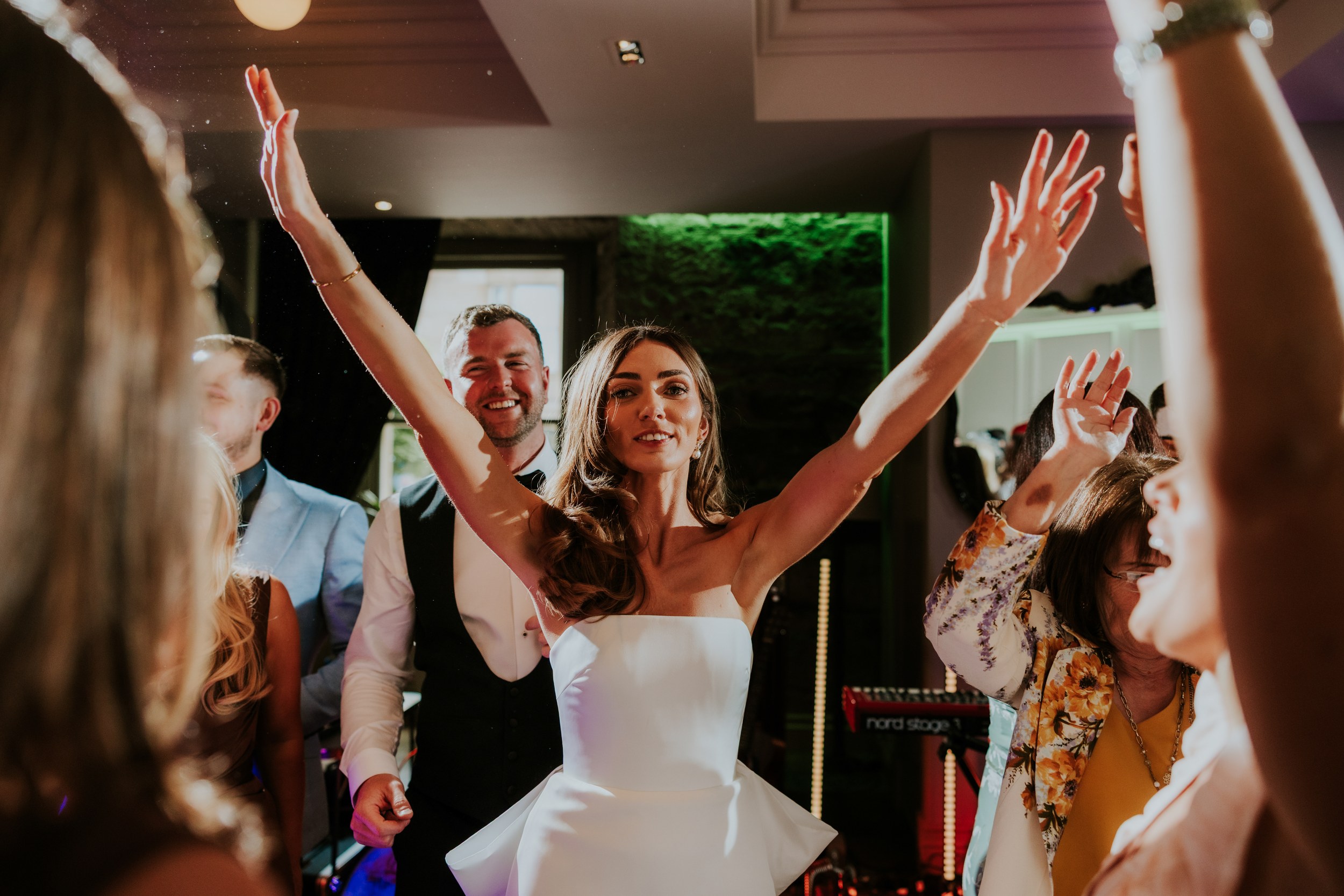 Citation Glasgow wedding photographer 83 Bride in a strapless dress with arms raised, groom and guests dancing and cheering at the reception.