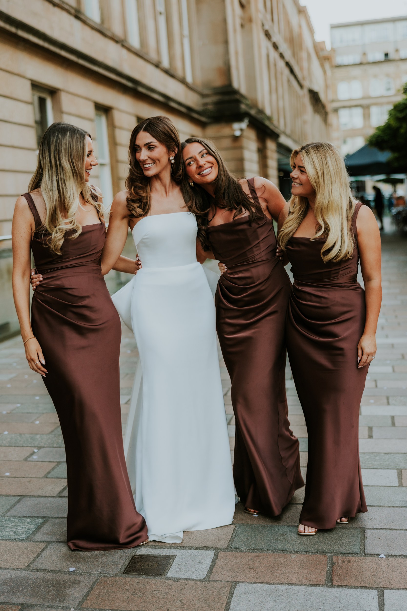 Citation Glasgow wedding photographer 92 Bride in a strapless white gown with three bridesmaids in brown satin dresses, arm‑in‑arm and smiling outside.