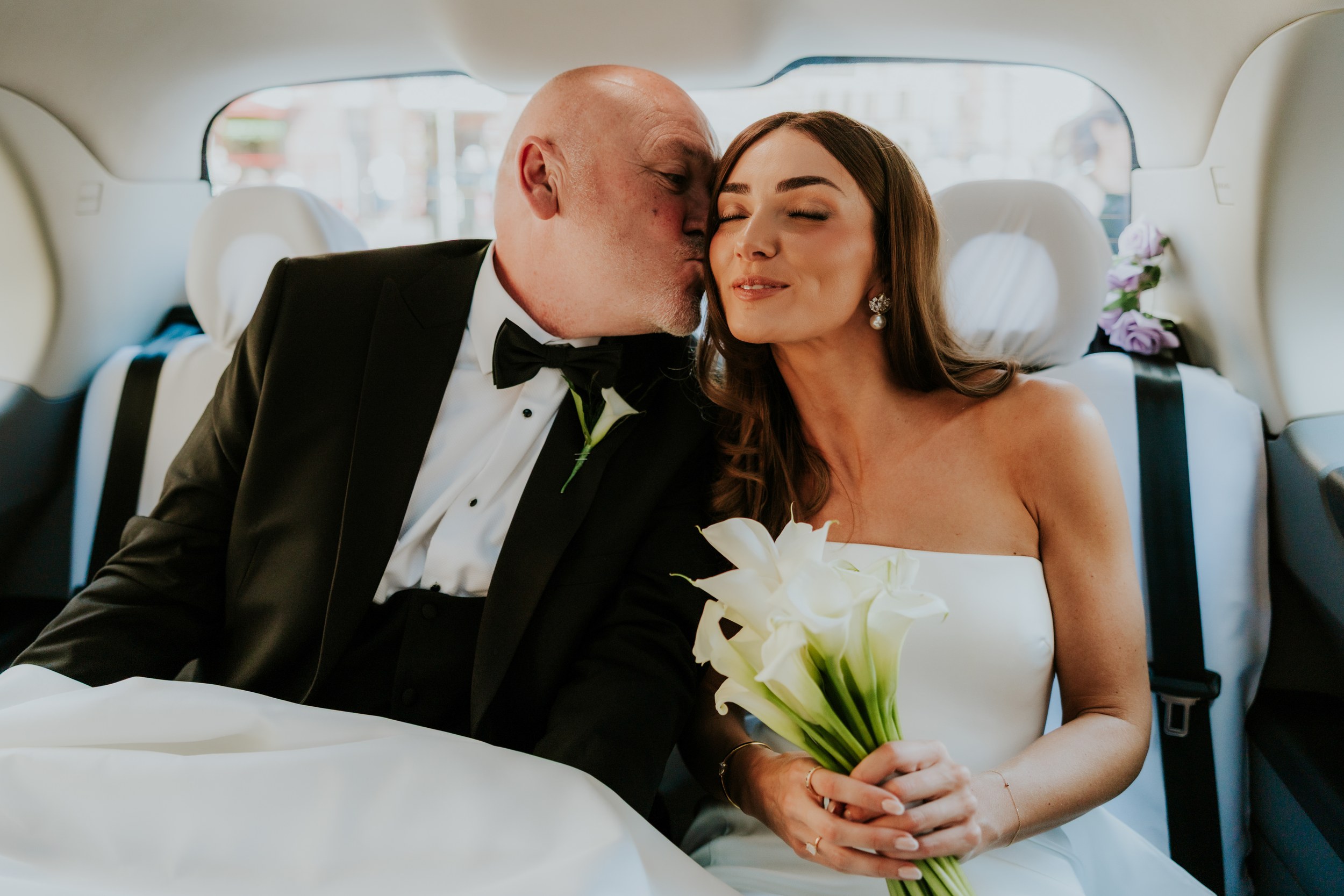 Citation Glasgow wedding photographer 20 Bride in strapless dress holding calla lilies as a man in a tuxedo kisses her cheek inside a car