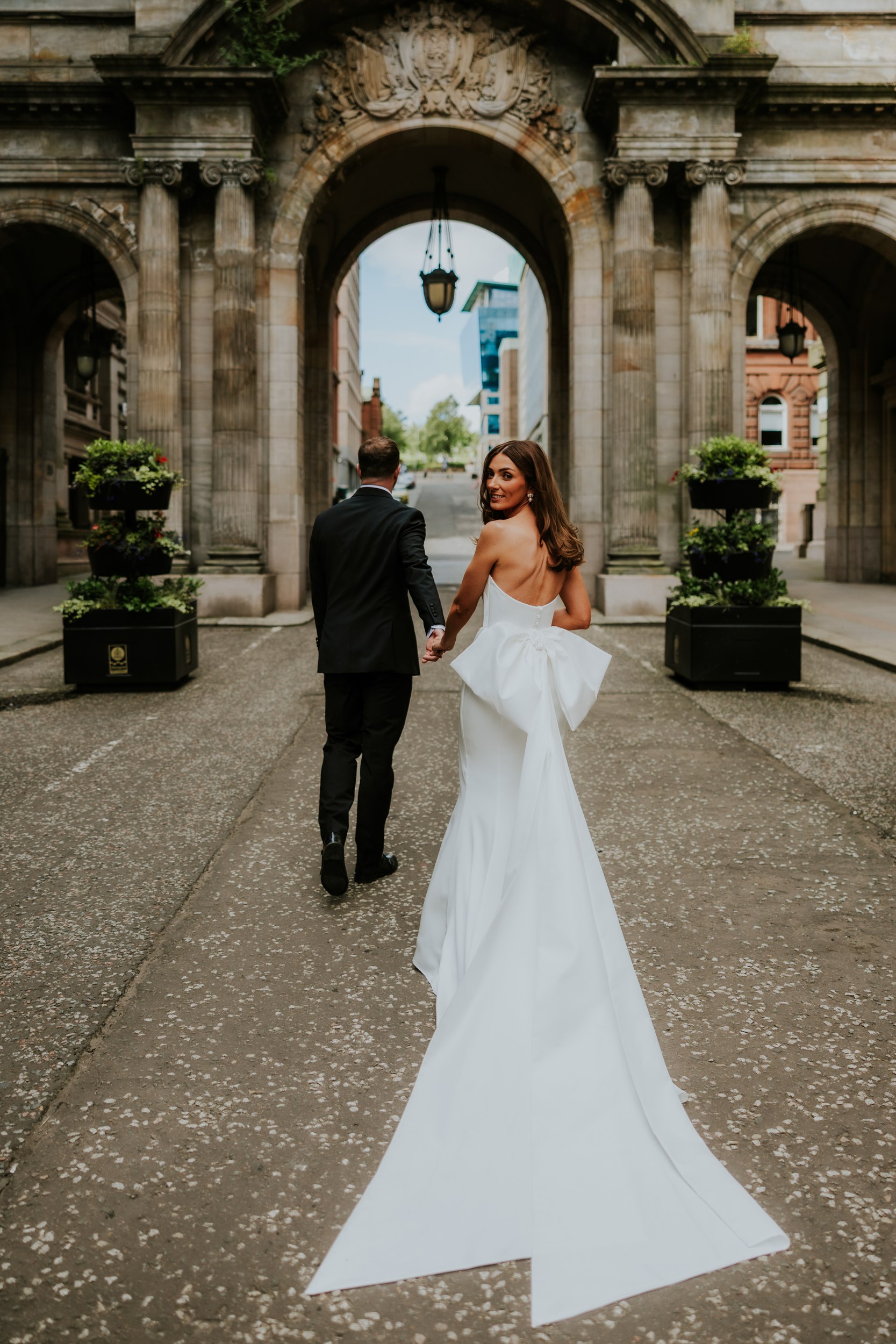 Citation Glasgow wedding photographer 52 Bride in strapless white gown looks back while holding groom's hand under a stone arch at Citation, Glasgow.