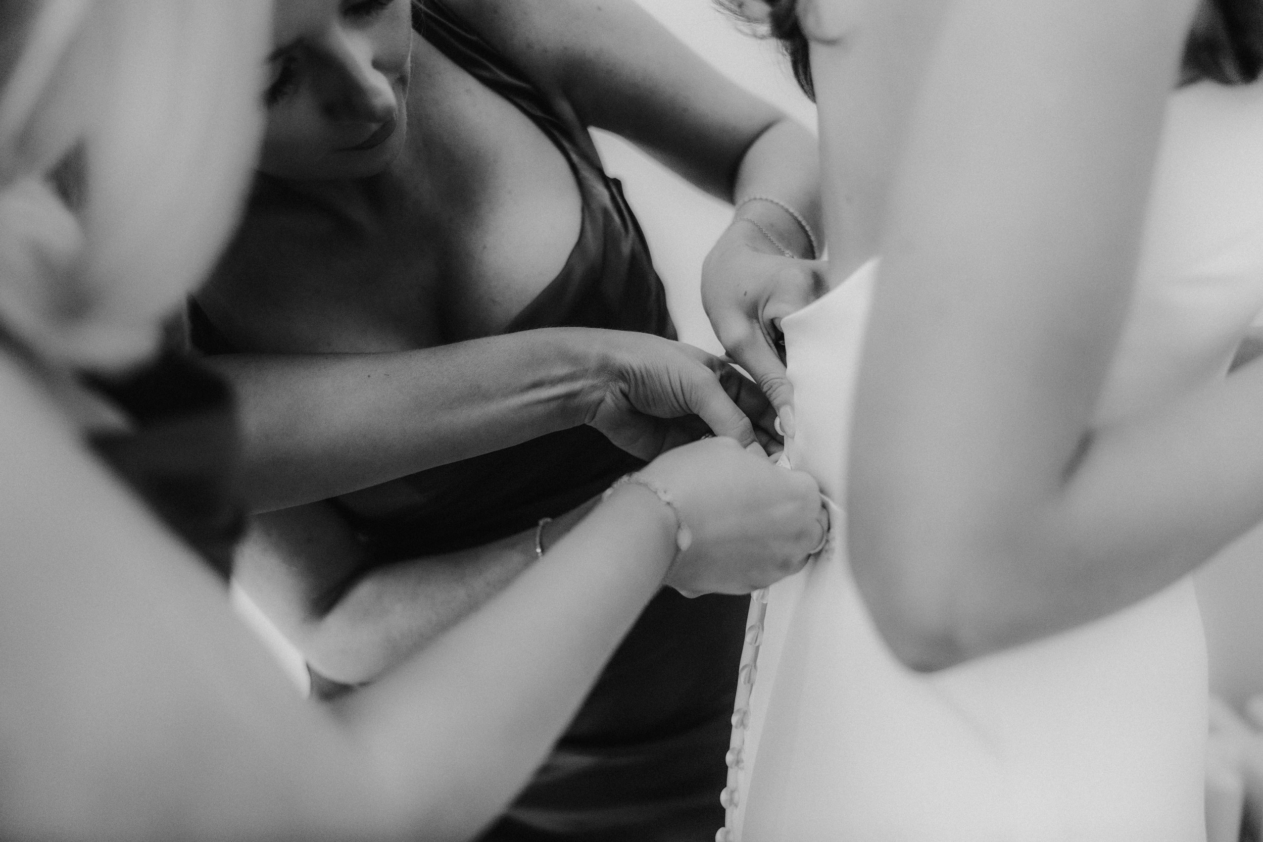 Citation Glasgow wedding photographer 14 Close-up of bridesmaids fastening buttons on a bride's wedding dress.