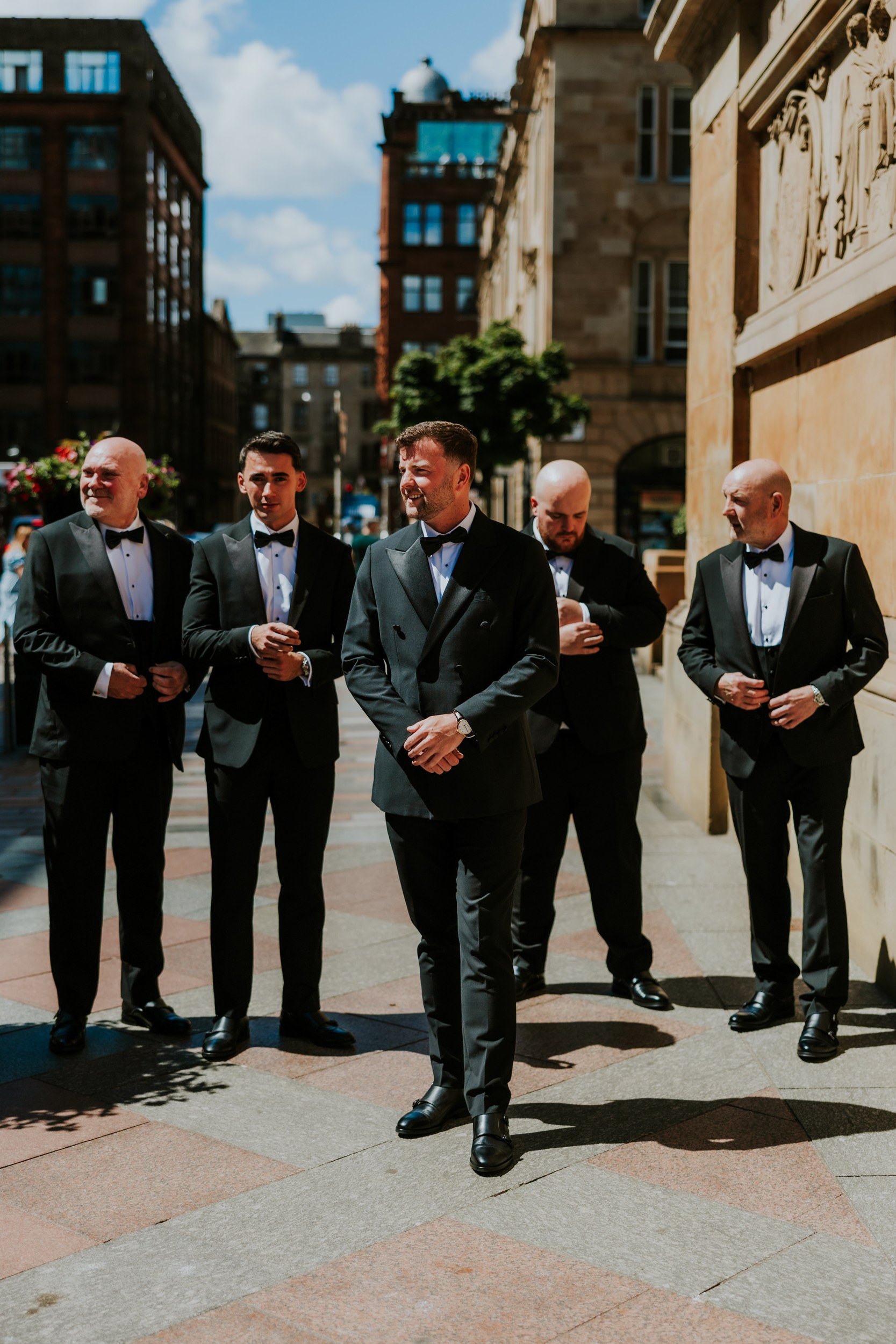 Citation Glasgow wedding photographer 7 Groom and four groomsmen in black tuxedos on a sunlit Glasgow street outside Citation Glasgow.
