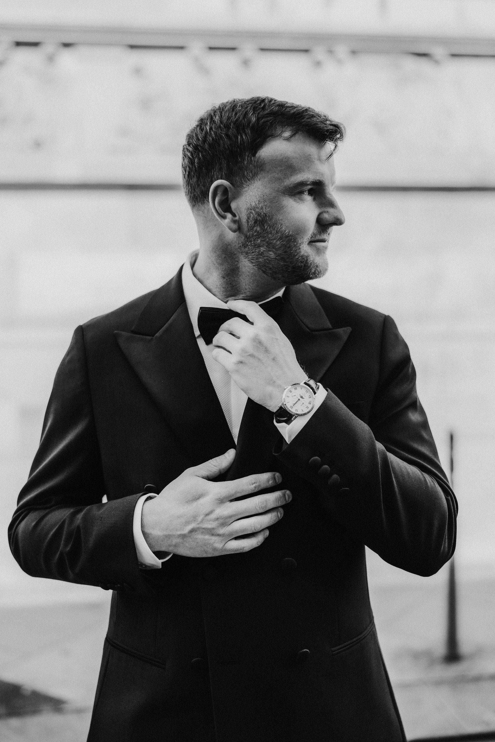 Citation Glasgow wedding photographer 6 Groom in tuxedo adjusts his bow tie, wearing a wristwatch, looking to his right (black-and-white portrait).