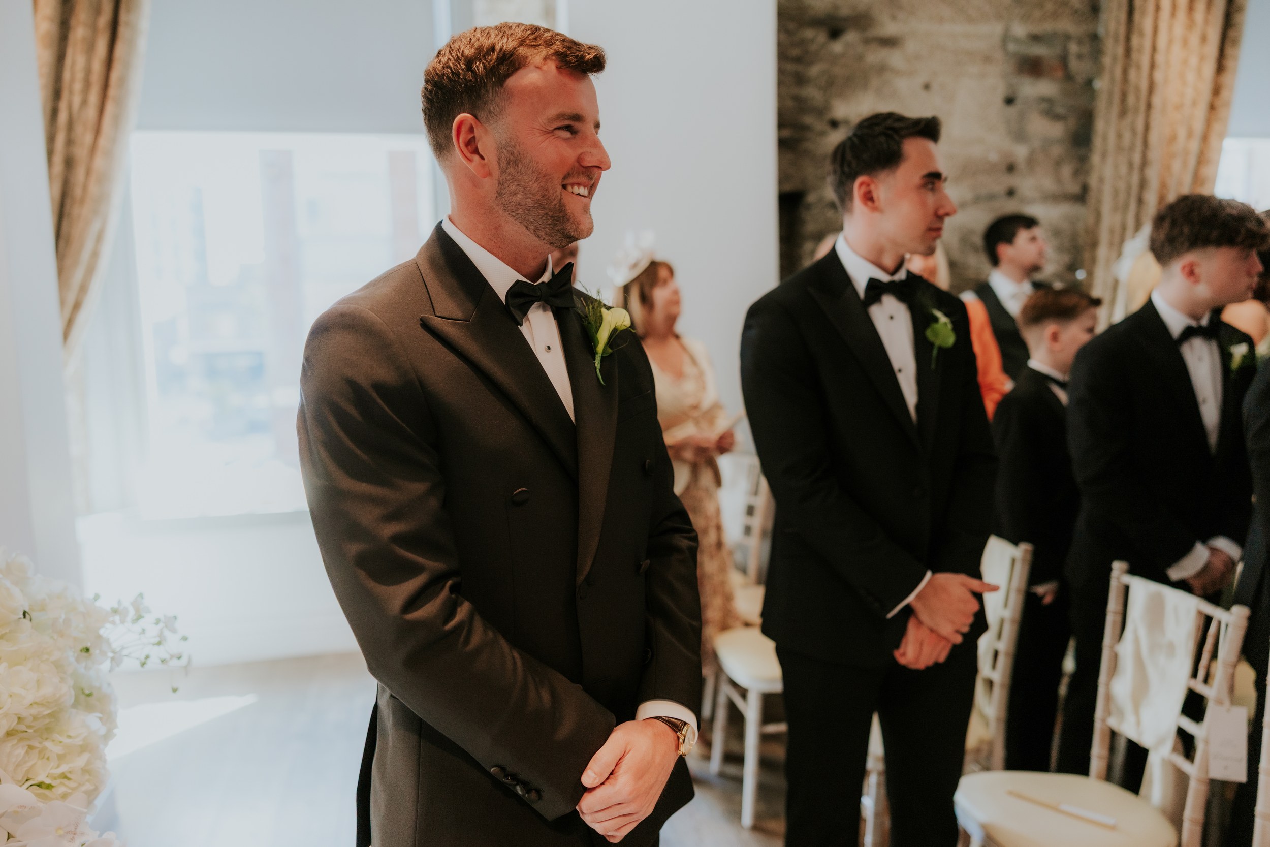 Citation Glasgow wedding photographer 24 Groom smiling in a tuxedo at the front of a wedding ceremony at Citation Glasgow, groomsmen beside him.