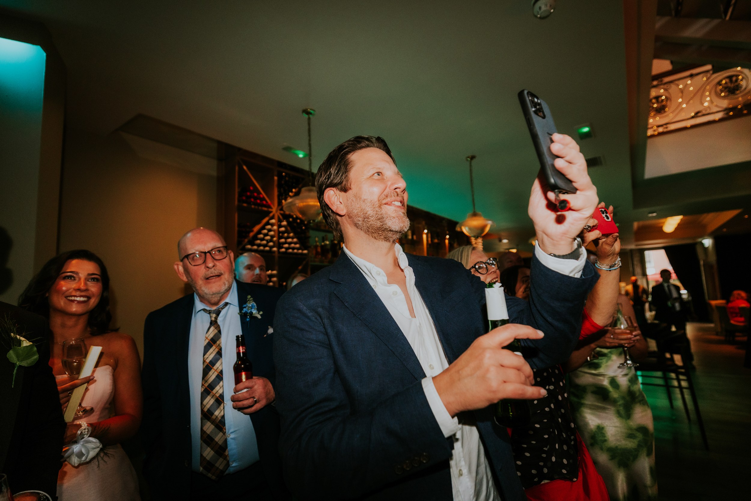 Citation Glasgow wedding photographer 81 Guests at a reception in Citation Glasgow, man raising a phone to take a photo while others smile and hold drinks.