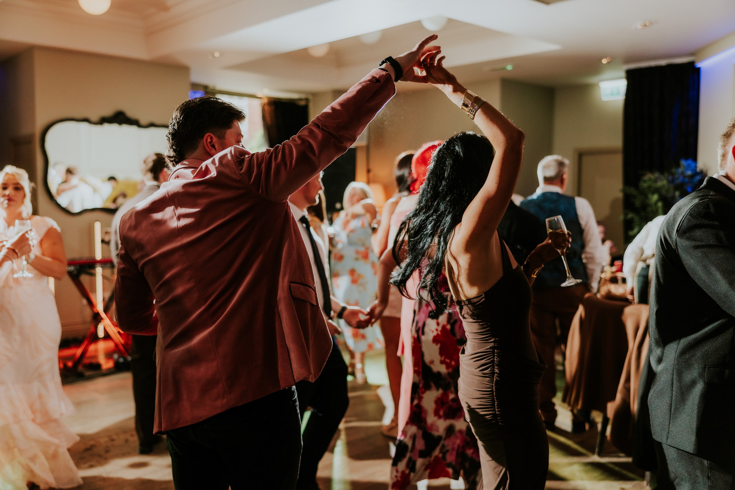 Citation Glasgow wedding photographer 80 Guests dancing at a wedding reception; a man in a pink jacket twirls a woman holding a champagne glass.