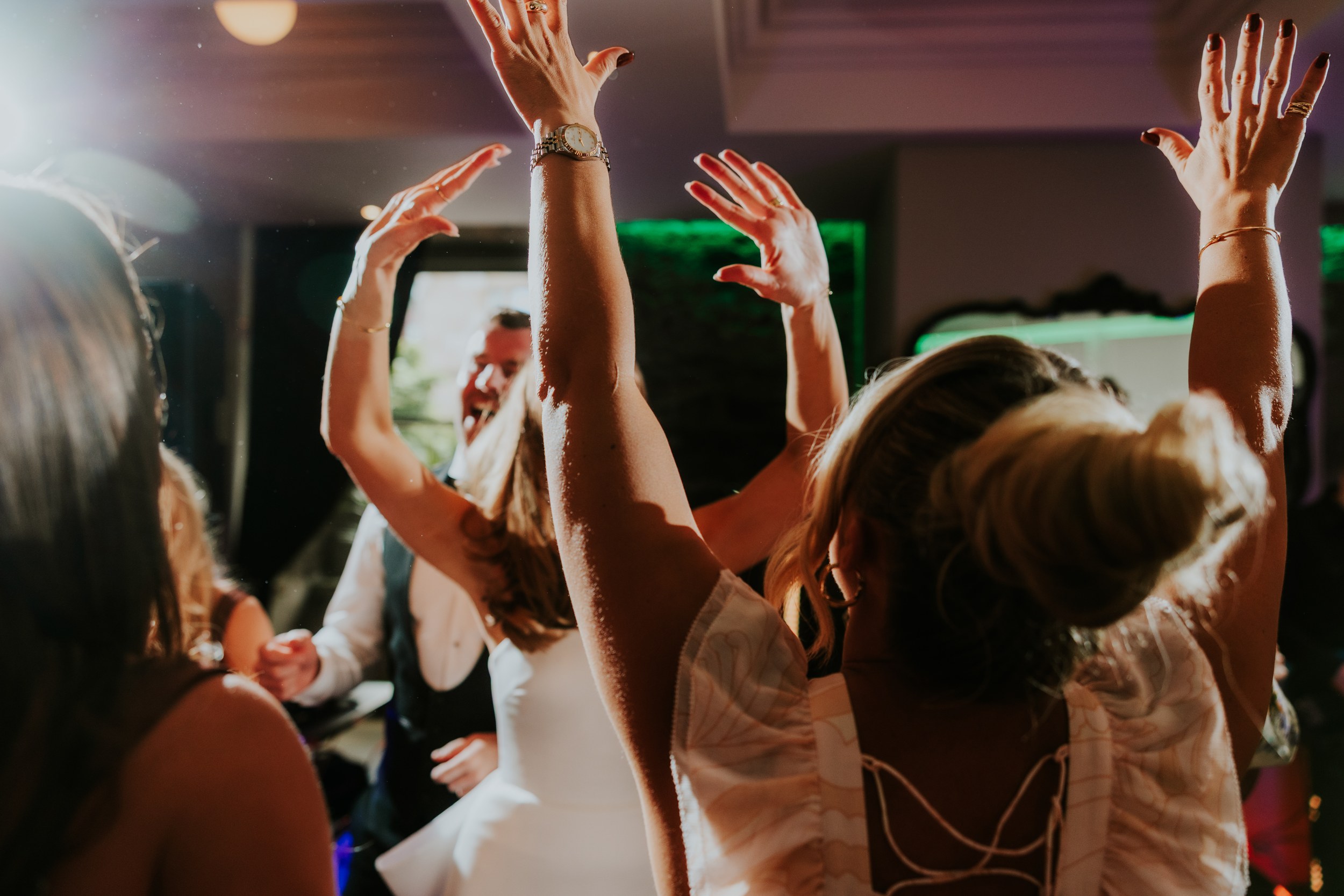 Citation Glasgow wedding photographer 82 Guests dancing with hands raised, a woman in a white dress visible on the dancefloor.