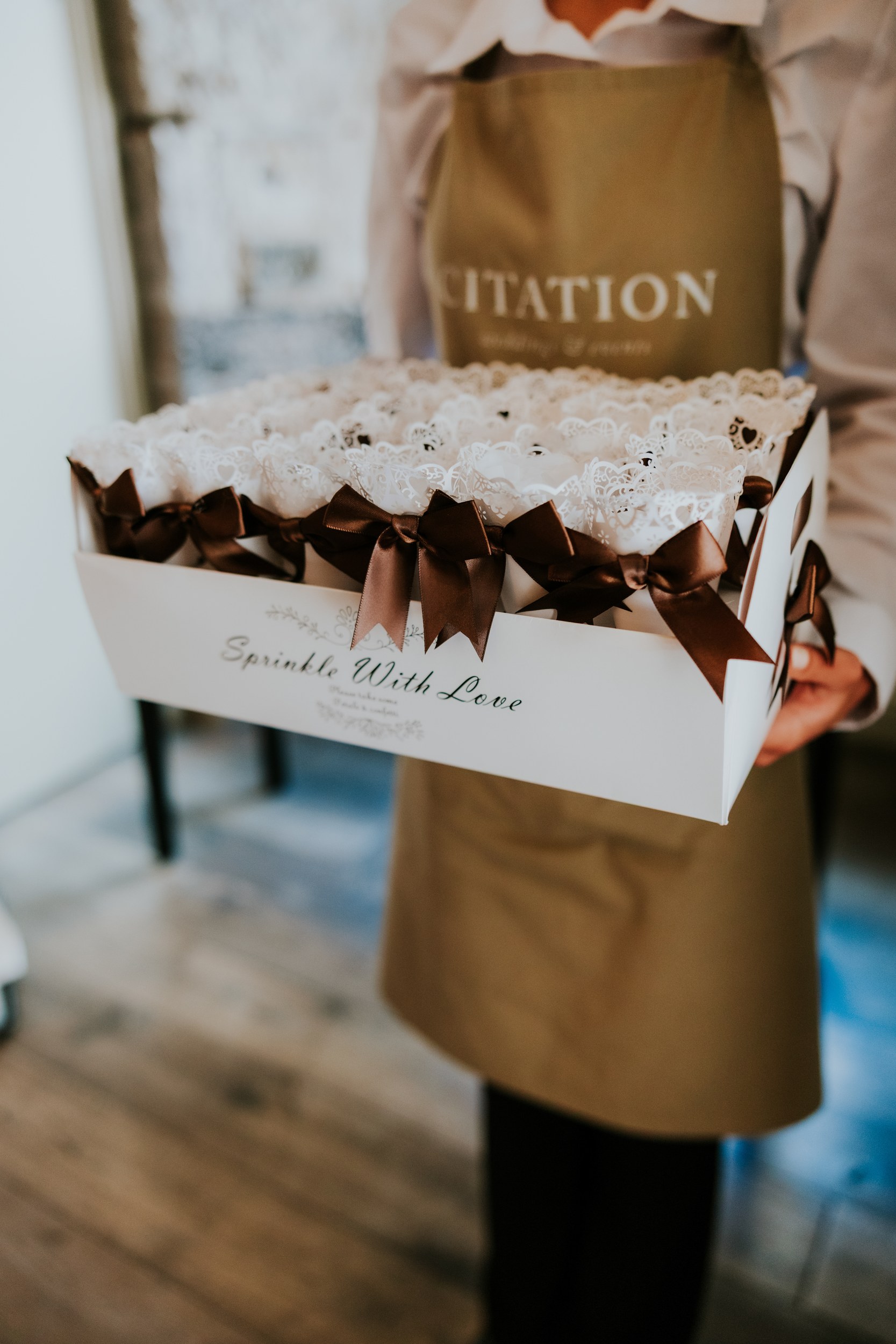 Citation Glasgow wedding photographer 37 Person holding a box of lace confetti cones tied with brown satin bows; apron labelled 'Citation' visible.
