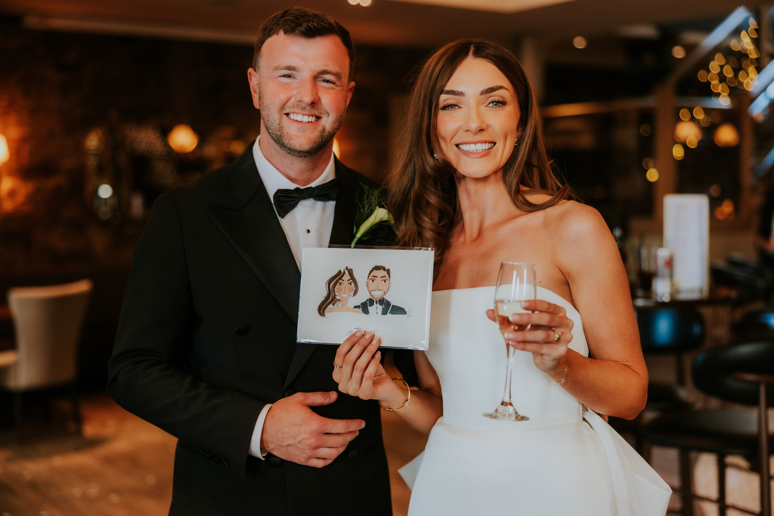 Citation Glasgow wedding photographer 68 Smiling bride and groom holding a caricature print and a champagne glass at an indoor reception.