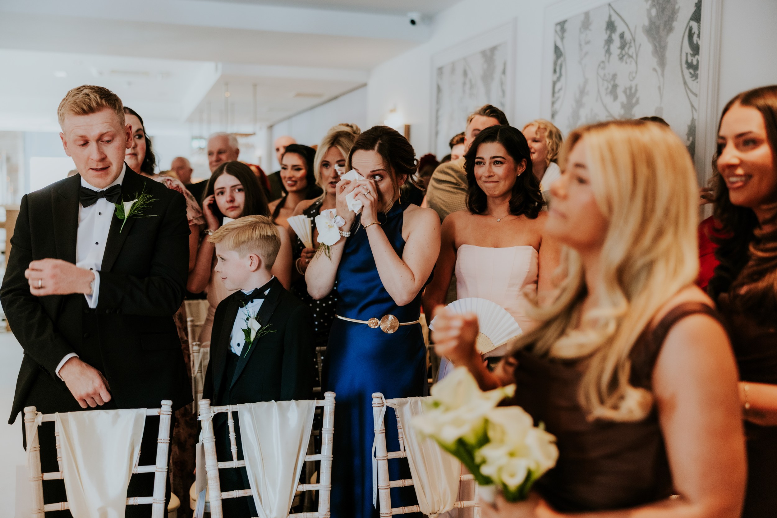 Citation Glasgow wedding photographer 27 Wedding guests standing indoors at Citation Glasgow, woman in blue wiping tears beside a smiling bridesmaid.