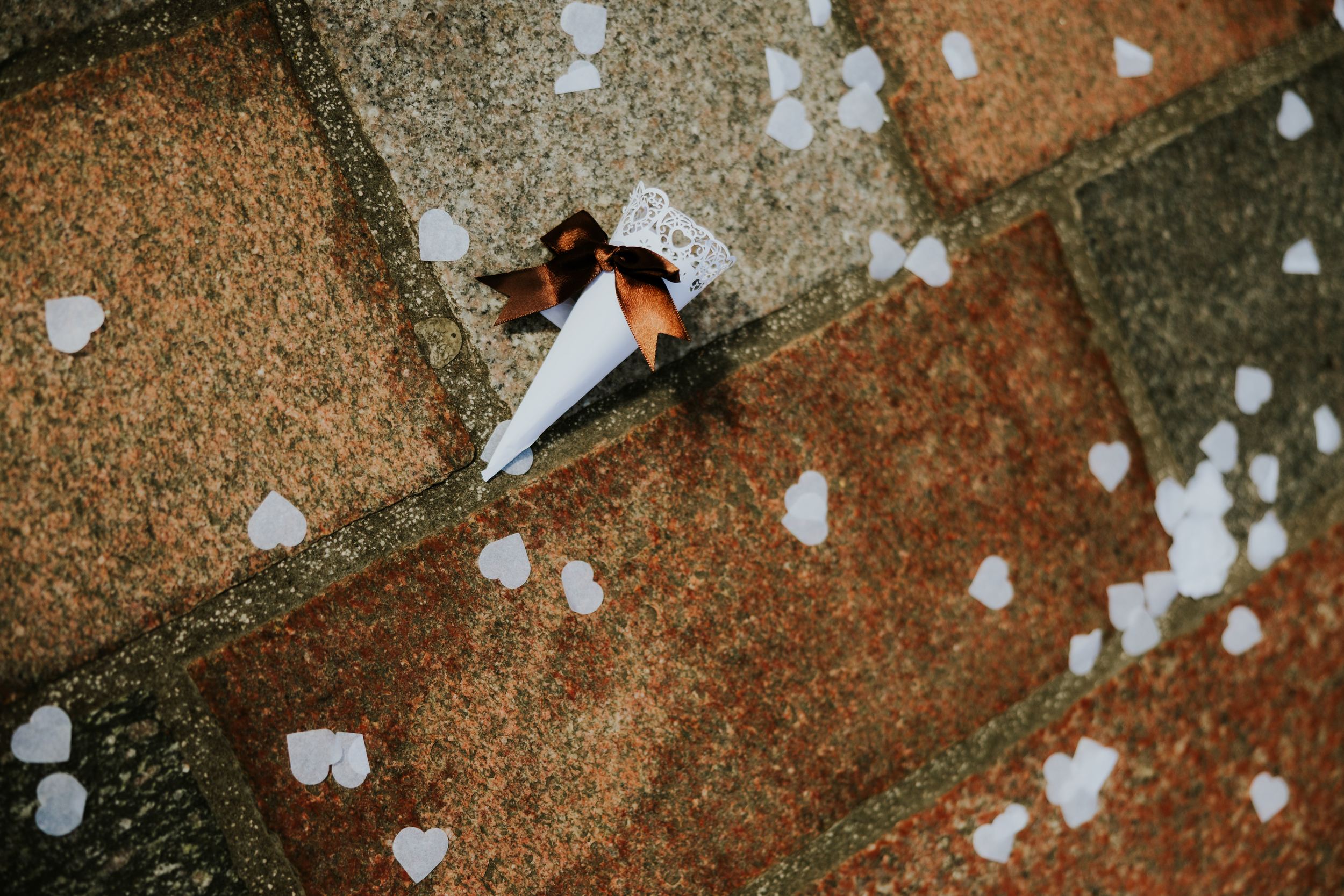 Citation Glasgow wedding photographer 42 White confetti cone with brown ribbon on stone paving, scattered white heart-shaped confetti.