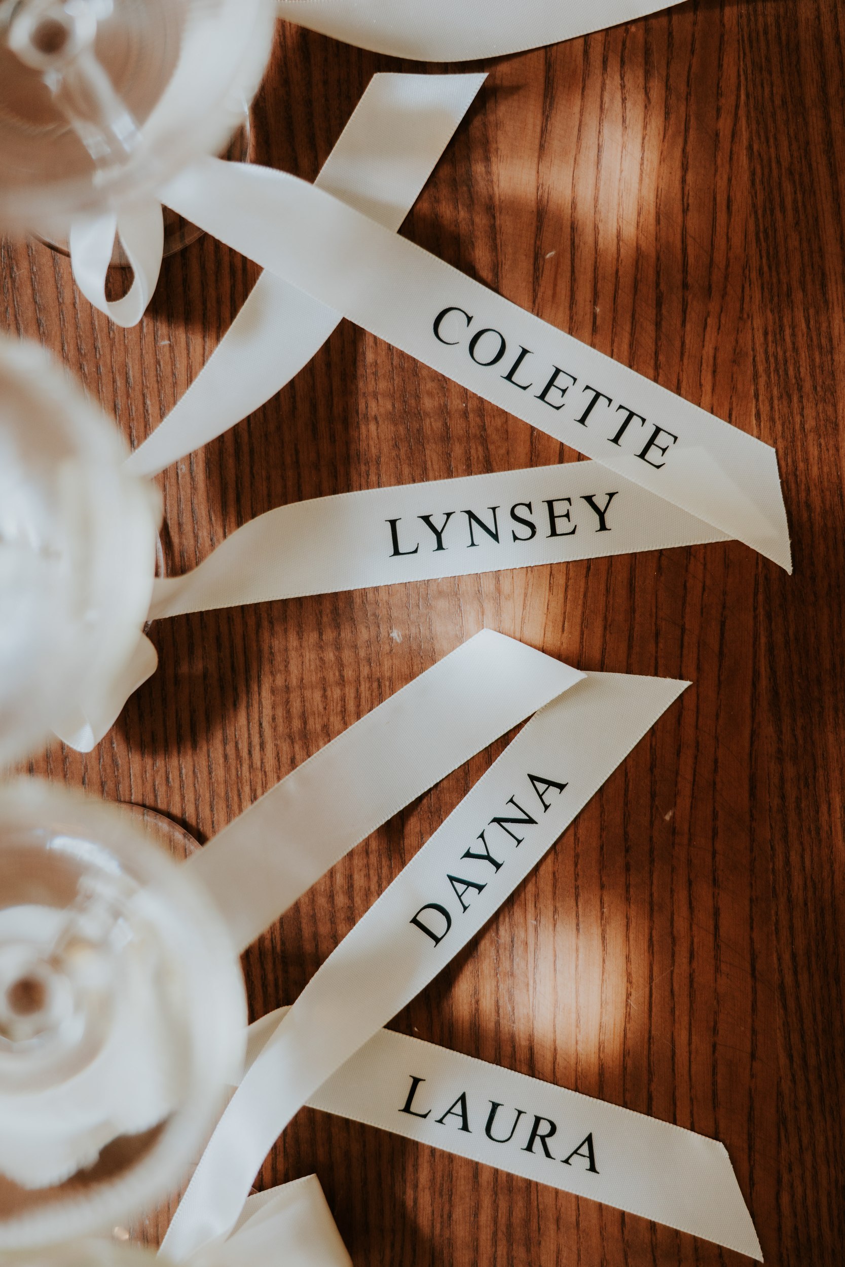 Citation Glasgow wedding photographer 12 White name ribbons reading 'COLETTE', 'LYNSEY', 'DAYNA' and 'LAURA' on a wooden table.