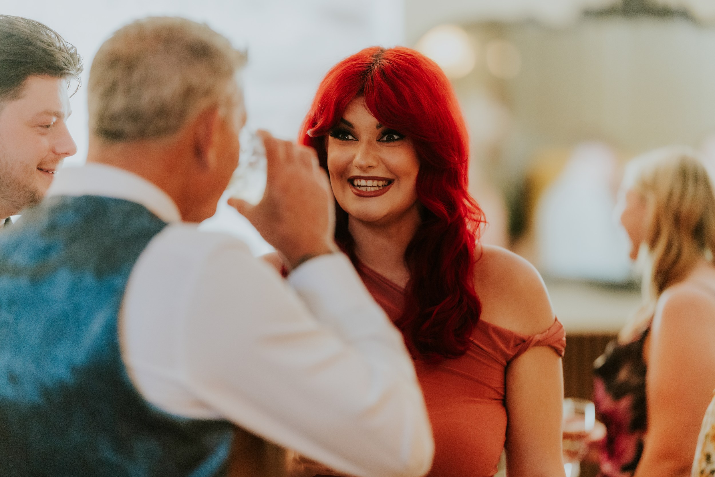 Citation Glasgow wedding photographer 61 Woman with bright red hair smiling and talking to a man holding a glass at a wedding reception.
