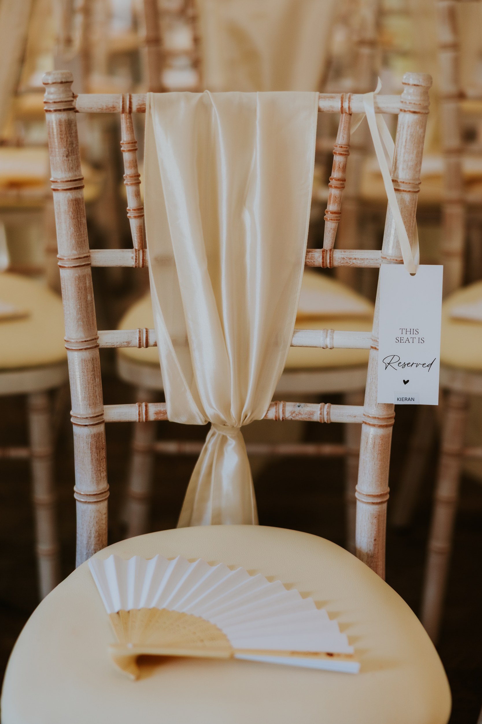 Citation Glasgow wedding photographer 2 Wooden Chiavari chair with cream satin sash, 'Reserved' tag and a paper fan on the seat.