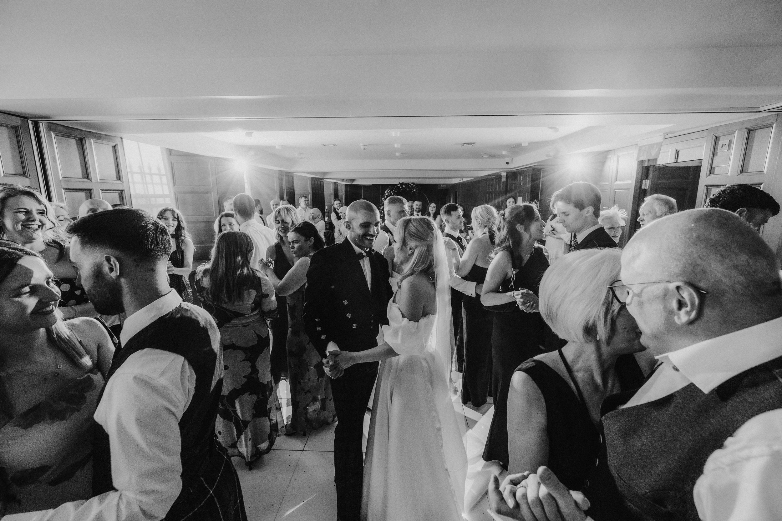 Bride and groom dancing in the middle of a crowded reception, guests holding hands around them.