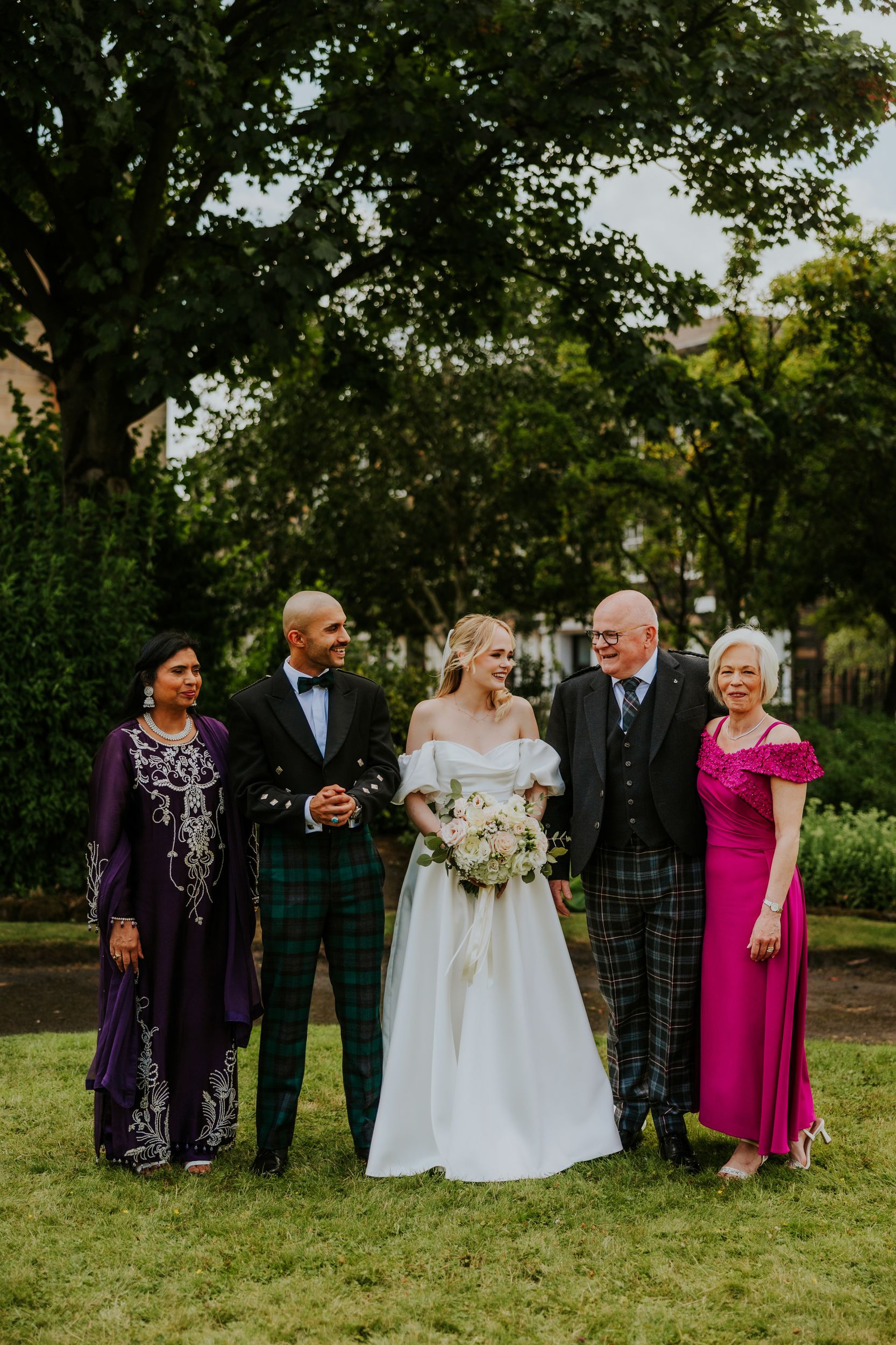 Bride Lauren and groom Zariq smiling with three guests under trees; bride in white holding bouquet.