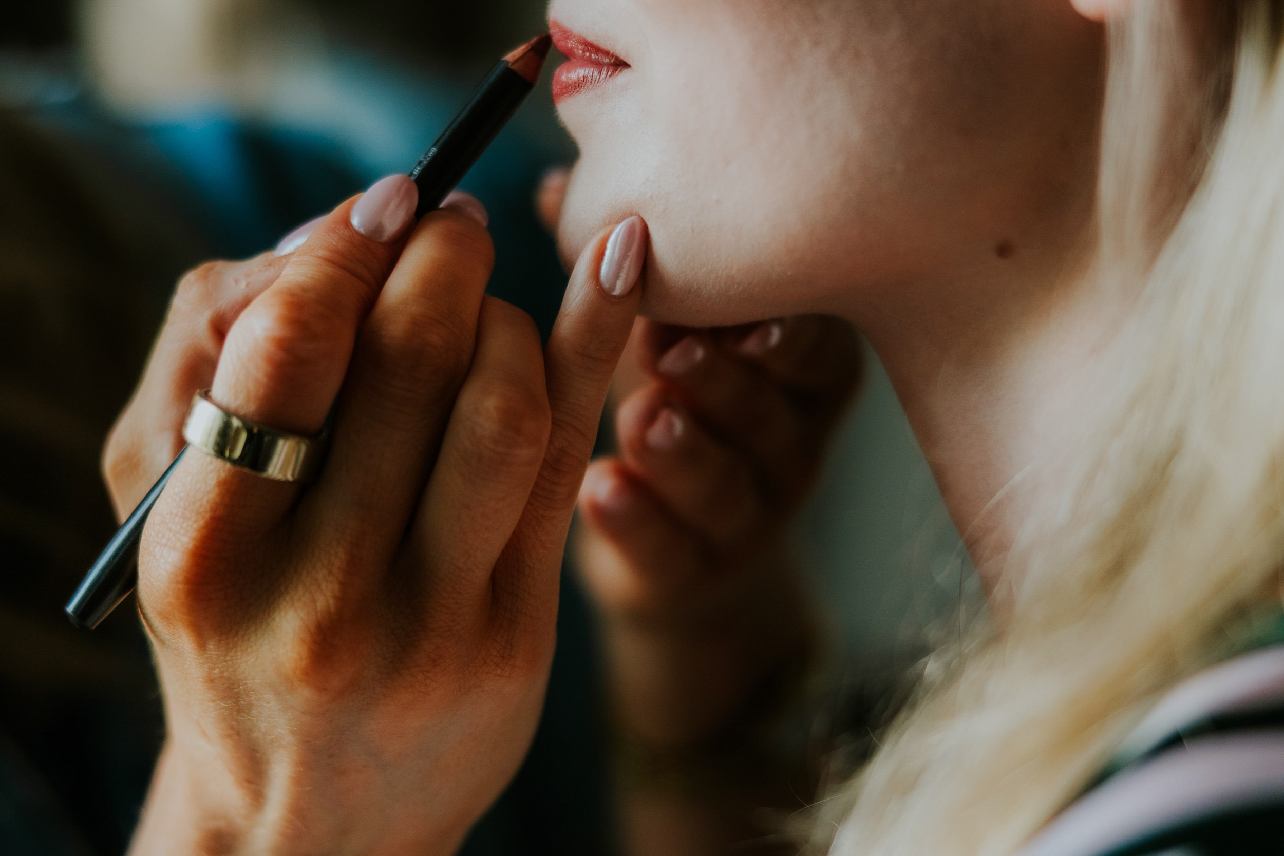 Close-up of a makeup artist applying lip liner to a bride's lips during wedding preparations.