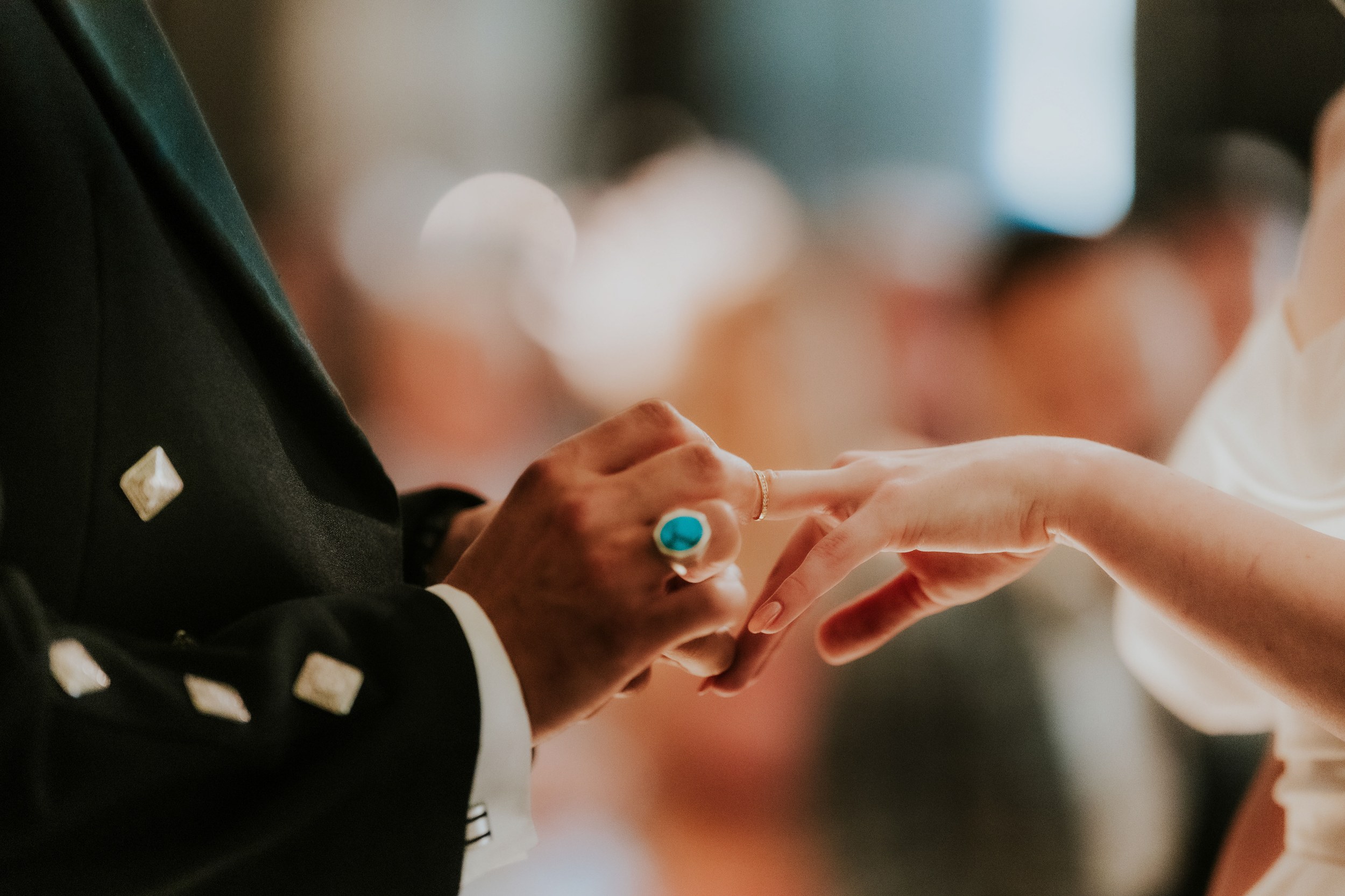 Close-up of hands as a gold wedding band is placed on a partner's finger during the ceremony.