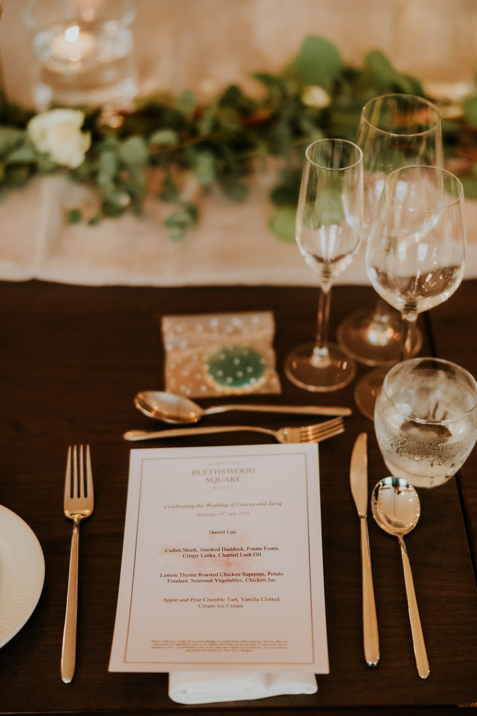 Table place setting with printed Blythswood Square wedding menu, cutlery, glassware and greenery runner.