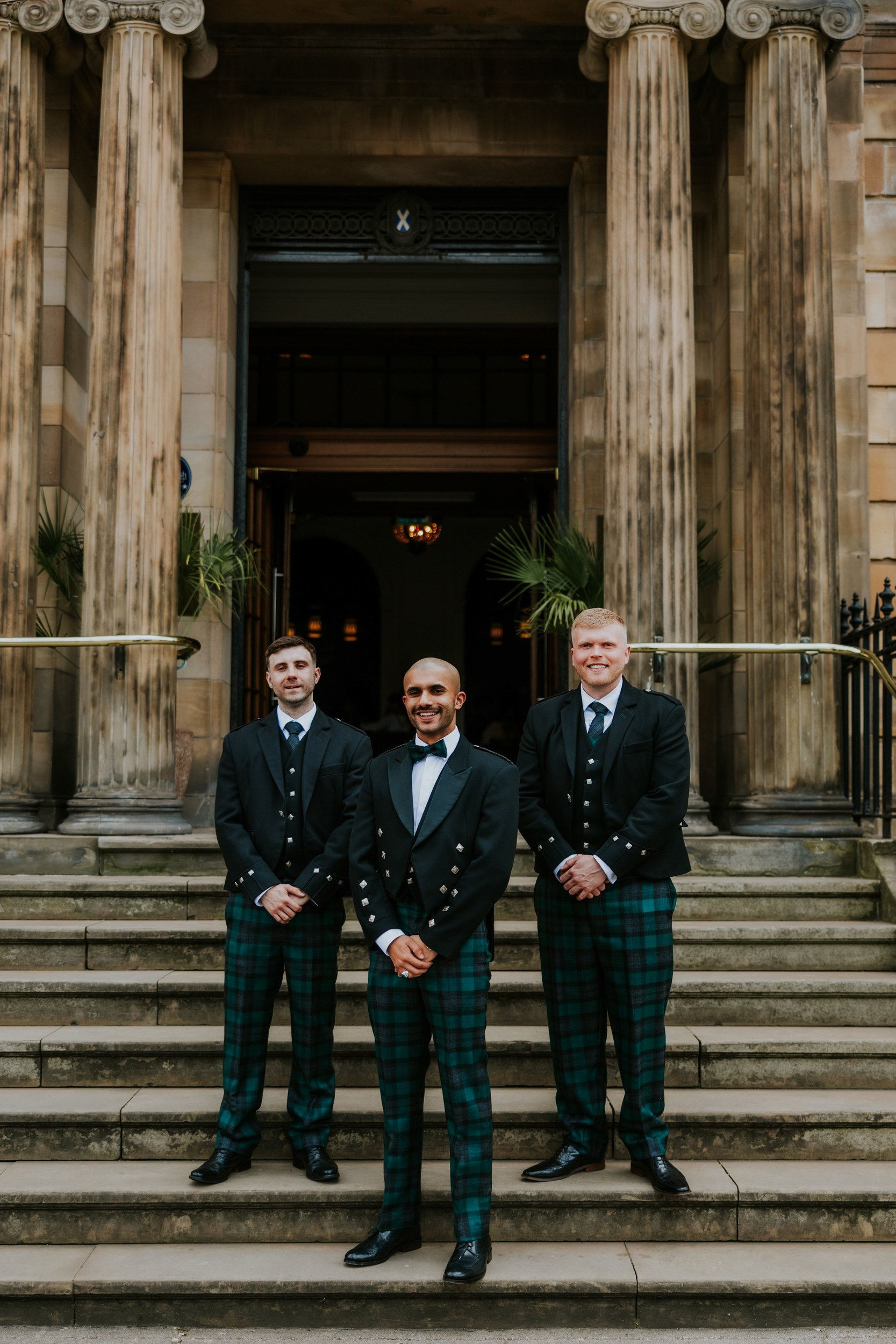 Three men in matching tartan kilts and formal jackets on stone steps outside Blythswood Hotel