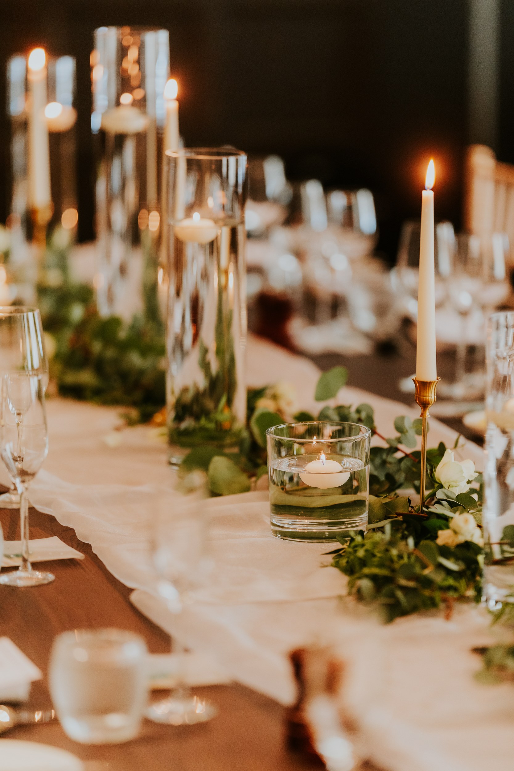 Wedding reception table with lit taper and floating candles, eucalyptus greenery and glassware.