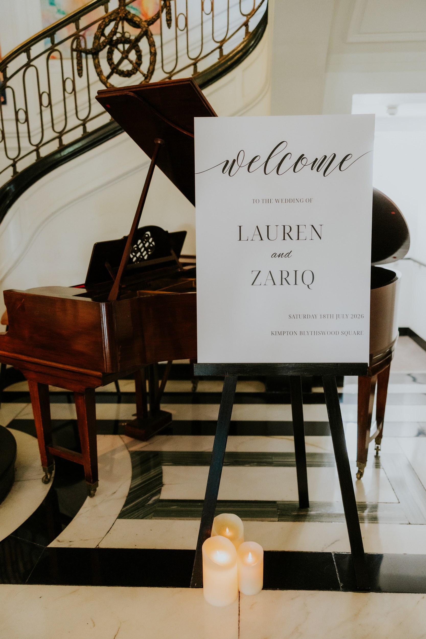 Welcome sign for Lauren and Zariq on an easel next to a grand piano and curved staircase at Kimpton Blythswood Square.