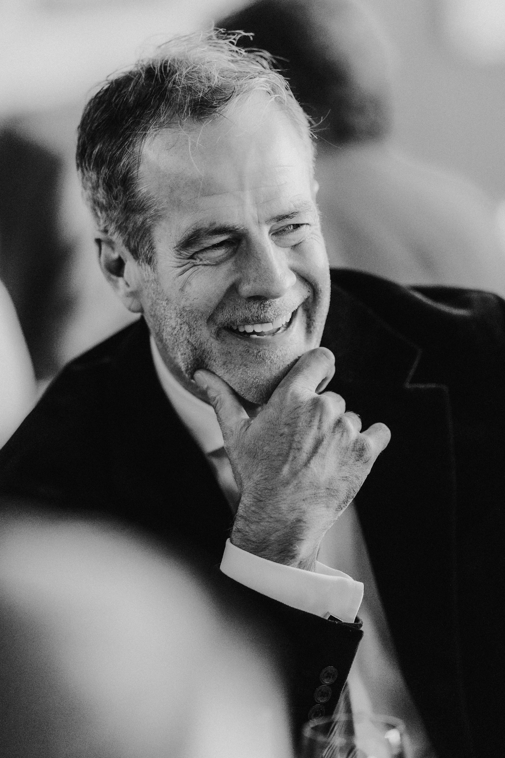 Black-and-white close-up of a smiling man with his hand on his chin, candid portrait.