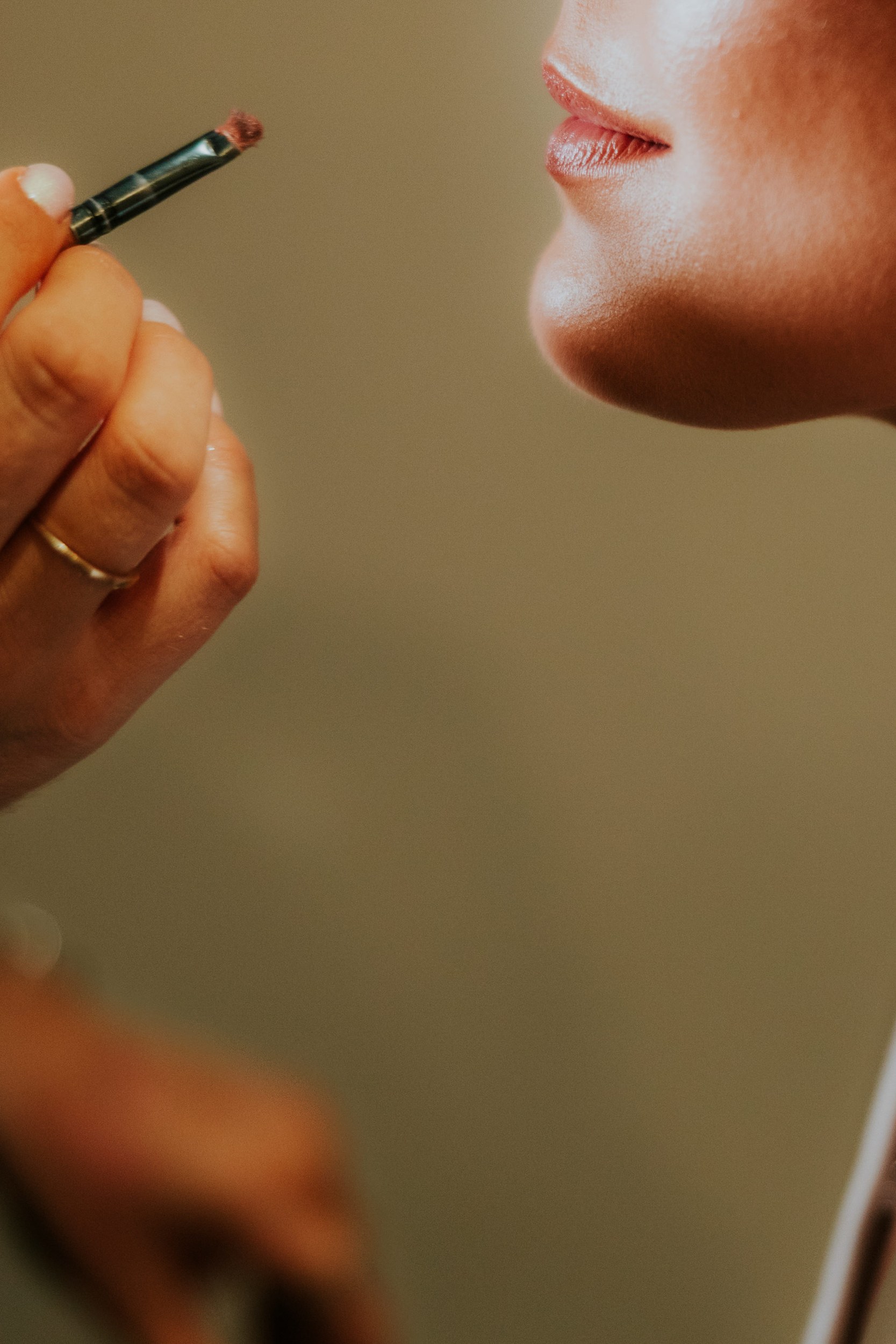 Close-up of a bride's lips and chin with a small makeup brush held nearby.
