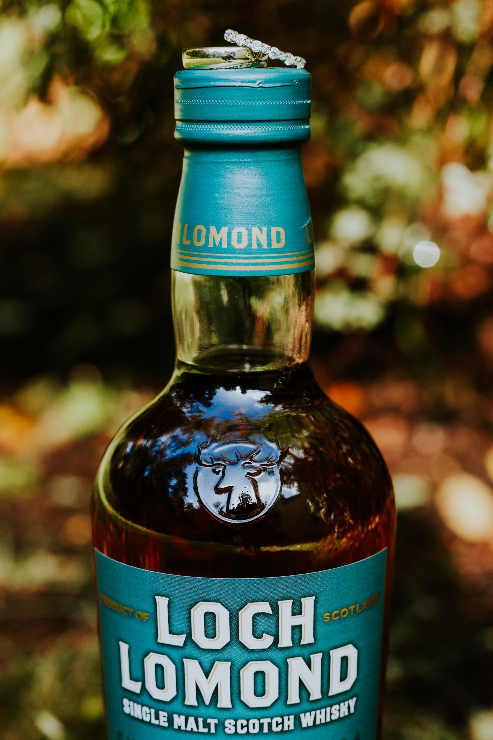 Close-up of a Loch Lomond whisky bottle with two wedding rings on the teal cap.