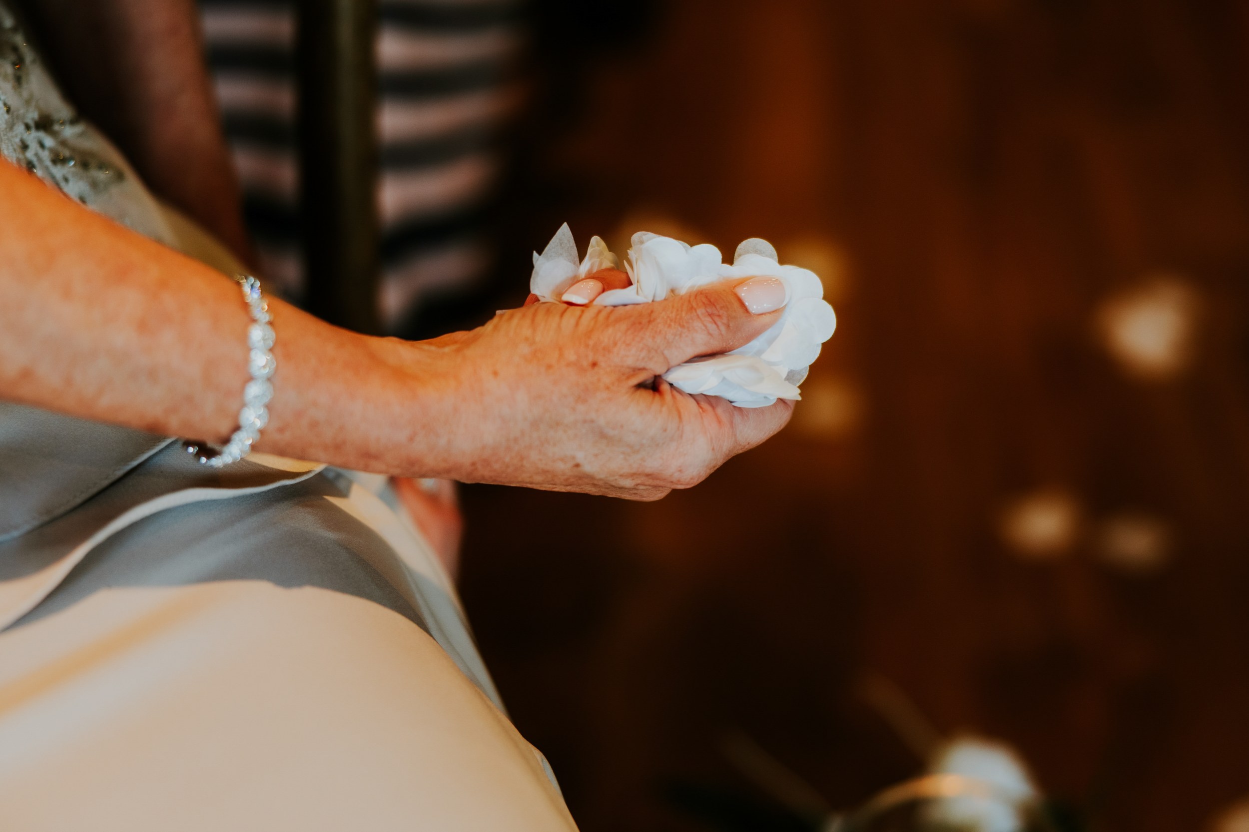 Close-up of hands holding white paper confetti petals, bracelet visible.