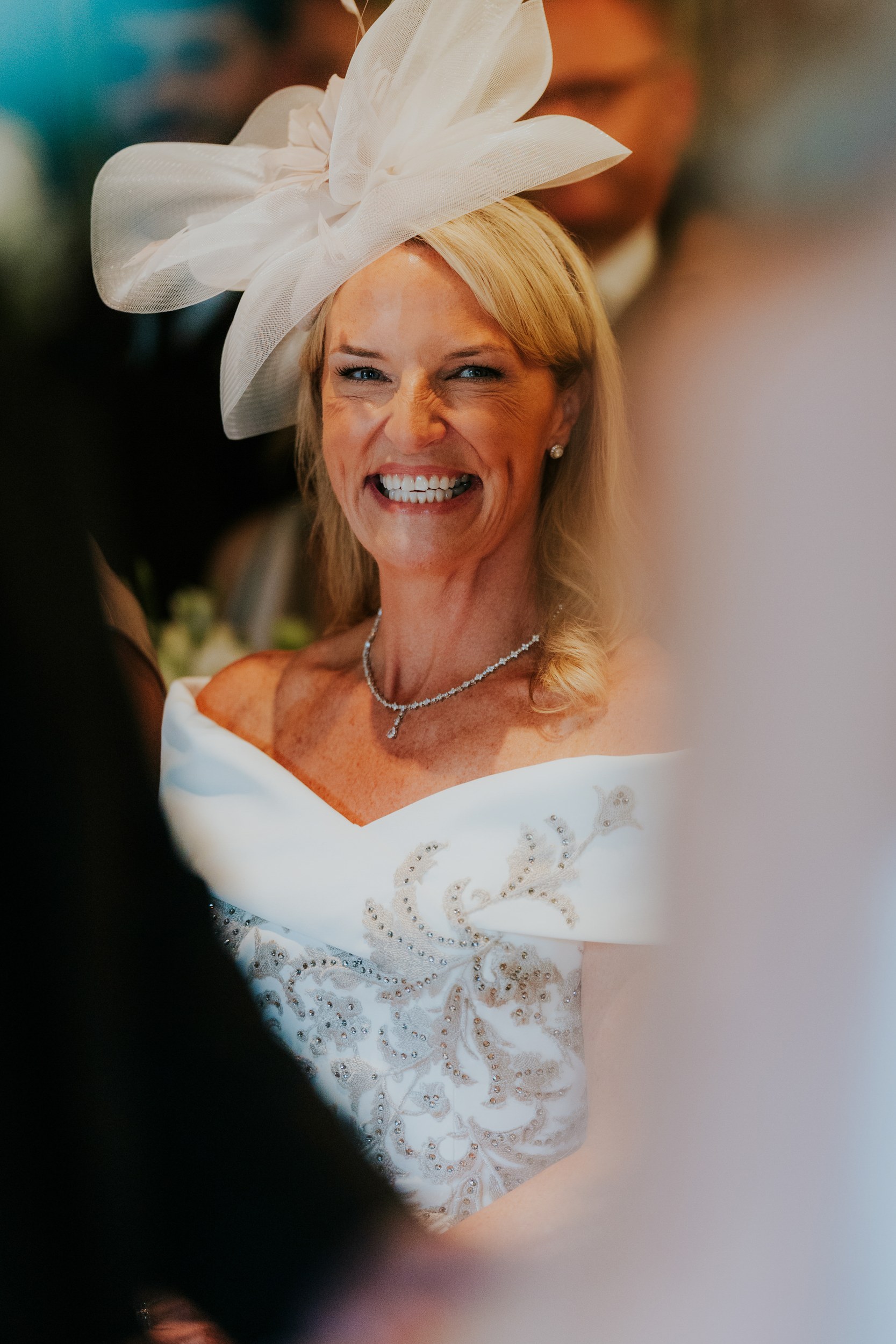 Close-up portrait of a smiling woman in a white off-shoulder dress and large white fascinator.