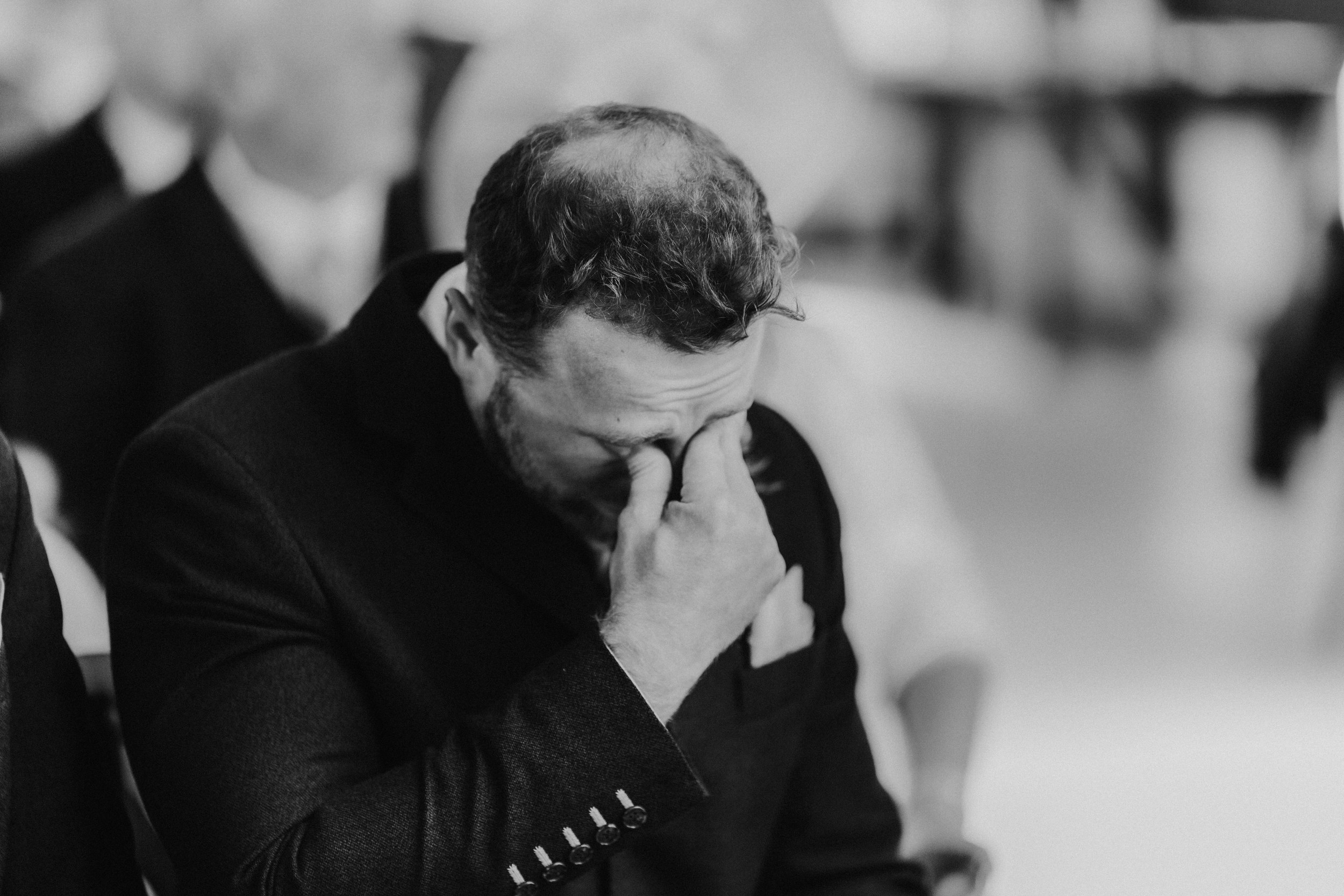 Daniel & Natalie’s Wedding at The Biscuit Factory 25 Black-and-white close-up of a man in a suit covering his face with his hand at a wedding ceremony.
