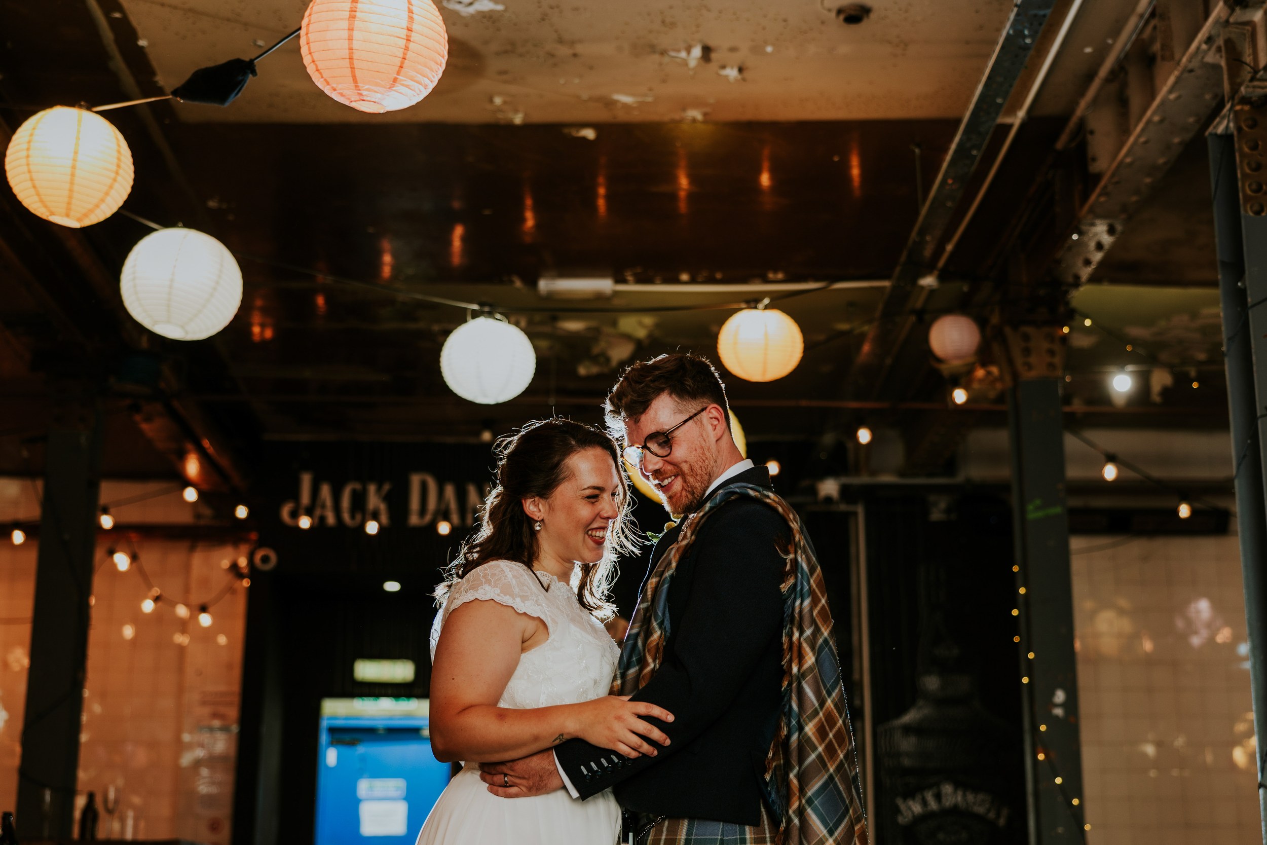 Daniel & Natalie’s Wedding at The Biscuit Factory 57 Natalie and Daniel smiling together beneath paper lanterns at The Biscuit Factory.