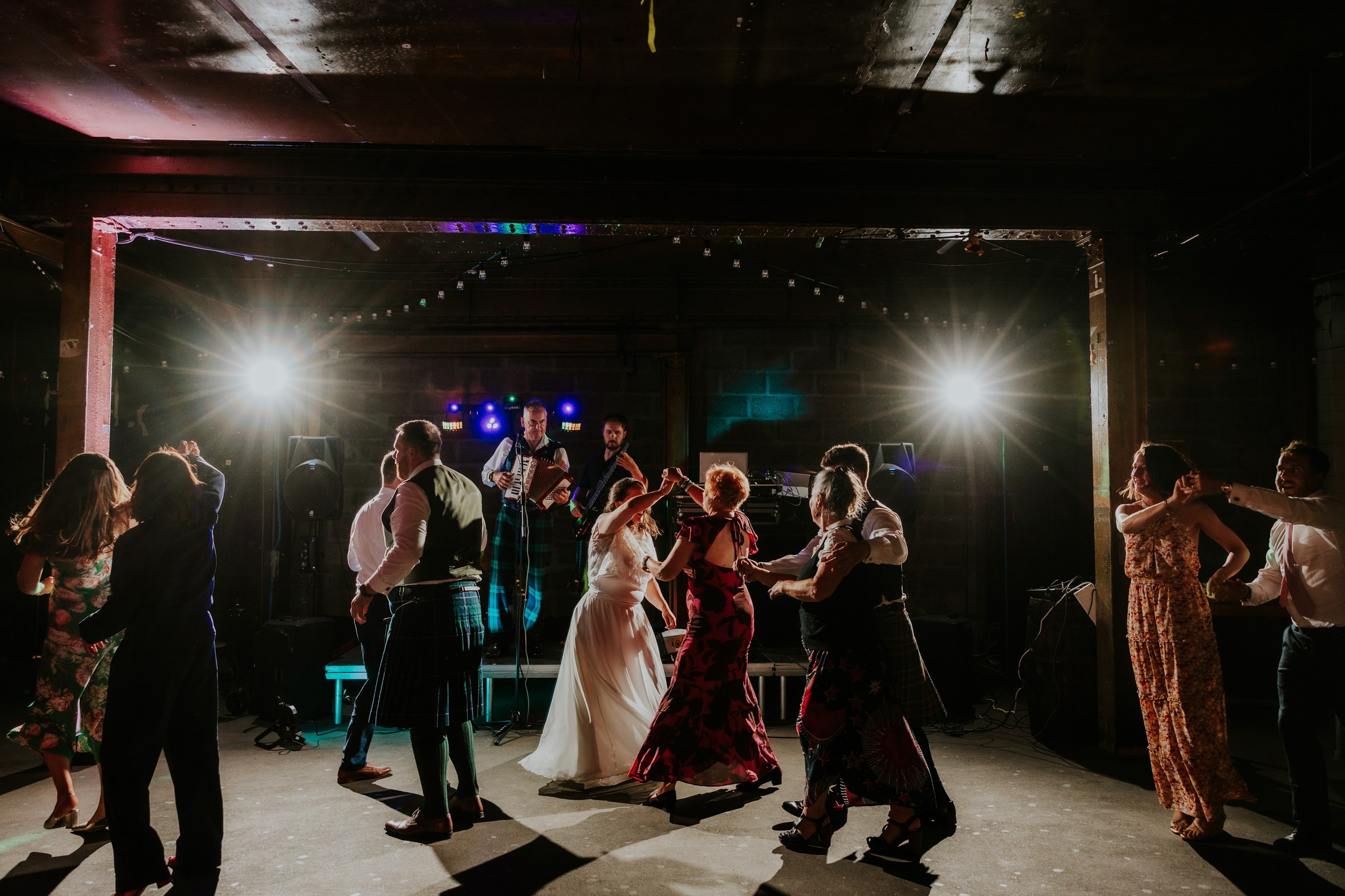 Daniel & Natalie’s Wedding at The Biscuit Factory 74 Bride and guests dancing to a live band under bright backlights at The Biscuit Factory reception.