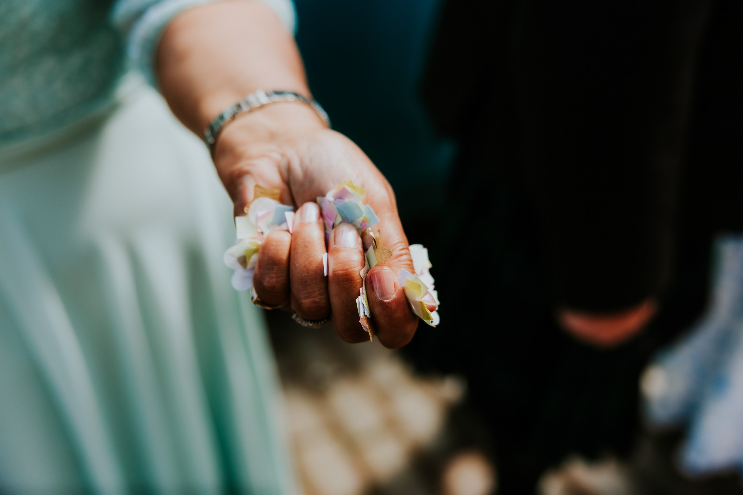 Daniel & Natalie’s Wedding at The Biscuit Factory 32 Hand holding pastel paper confetti with bracelet and pale green dress visible