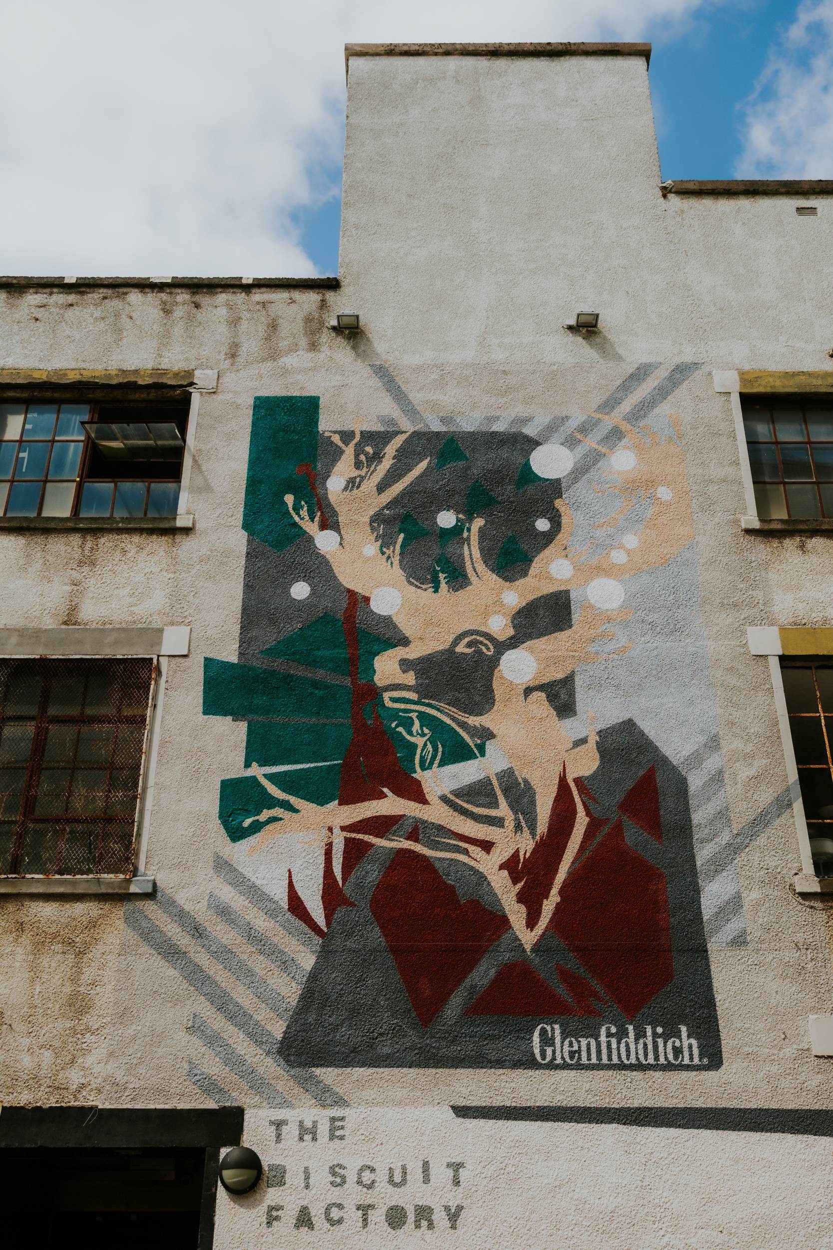 Daniel & Natalie’s Wedding at The Biscuit Factory 1 Mural of a stag and Glenfiddich ad on The Biscuit Factory exterior wall with two windows.