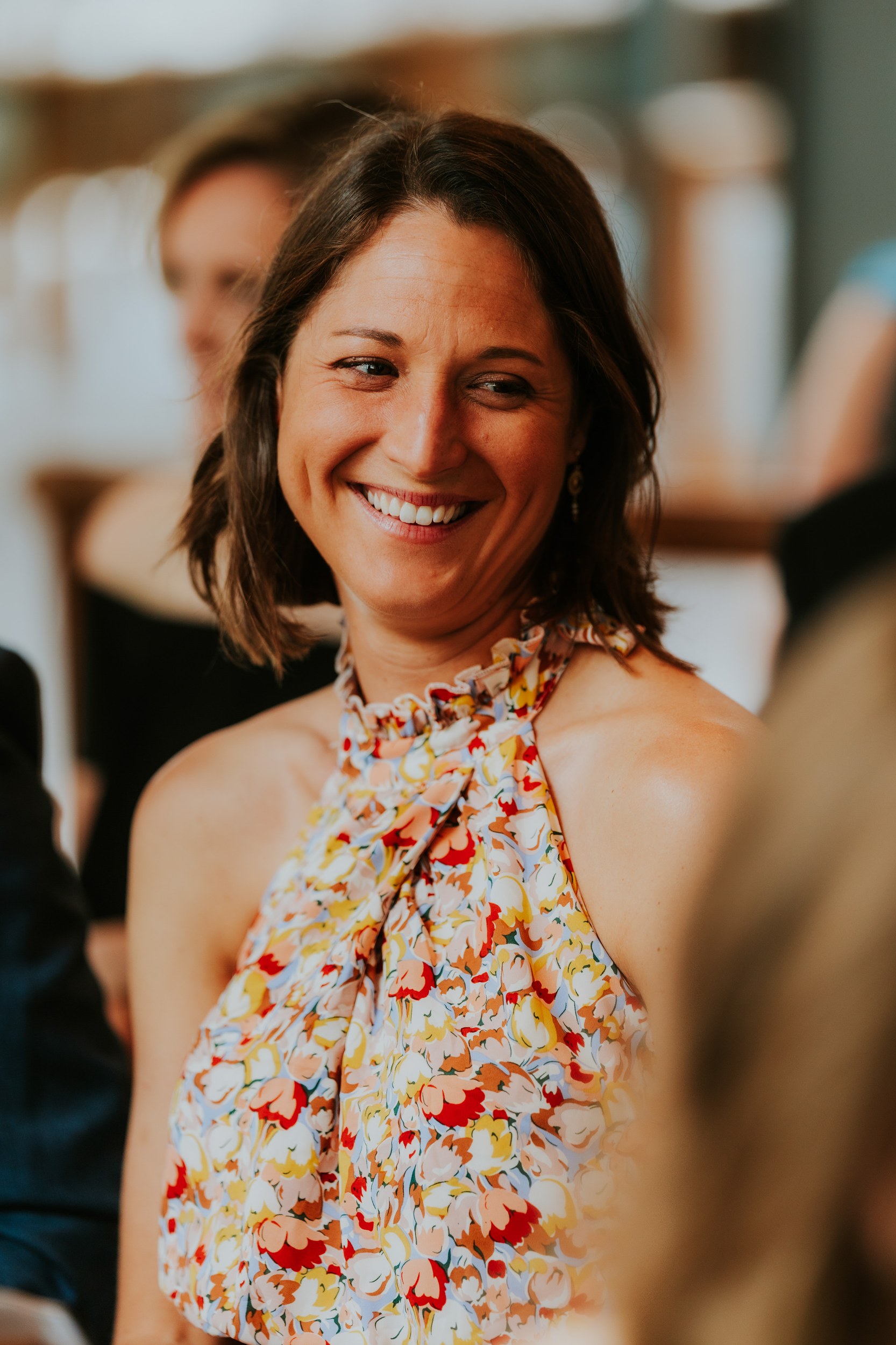 Daniel & Natalie’s Wedding at The Biscuit Factory 16 Smiling woman in a colourful floral halter dress at a wedding reception.