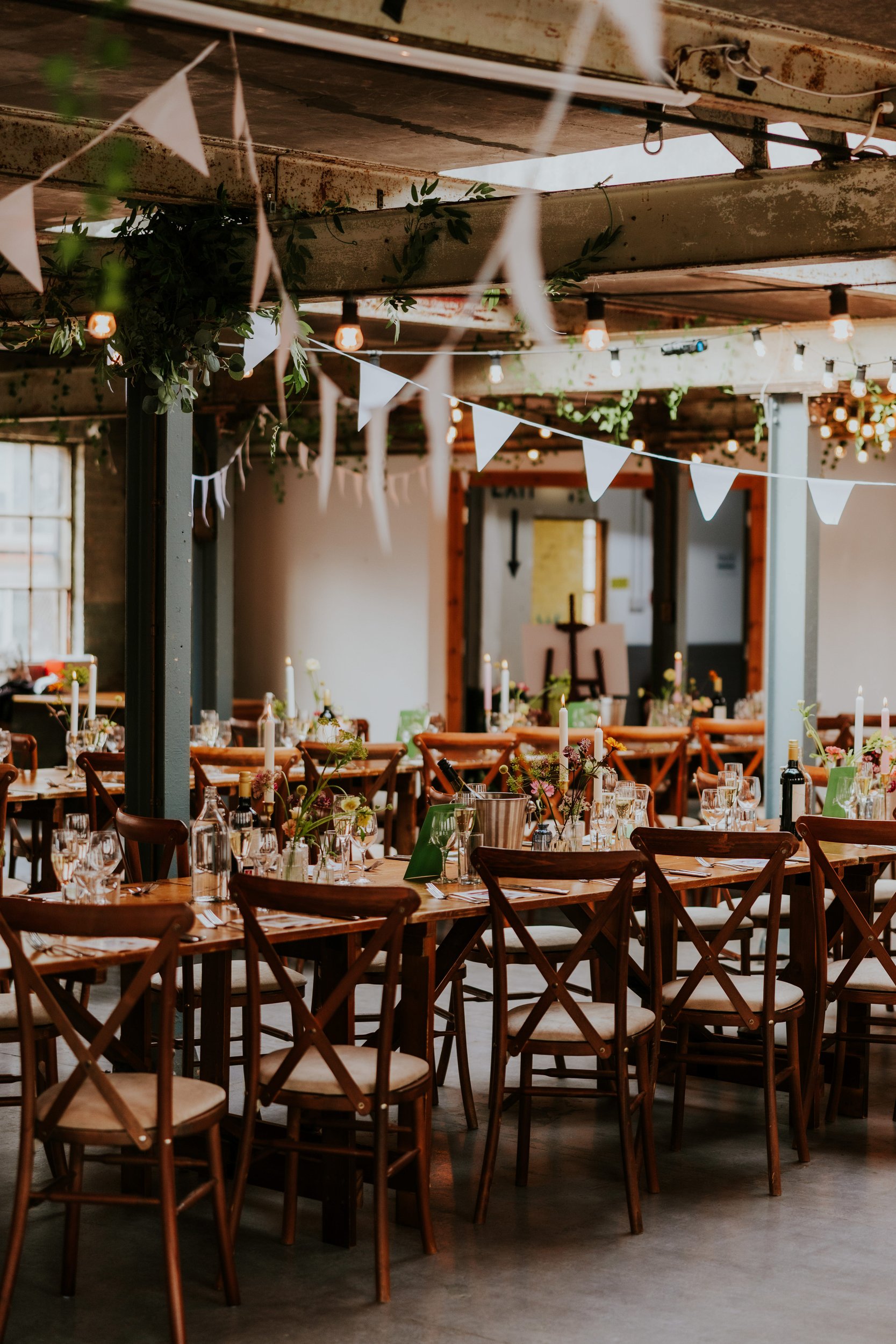 Daniel & Natalie’s Wedding at The Biscuit Factory 56 Wedding reception tables with bunting, hanging bulbs and foliage in an industrial venue.